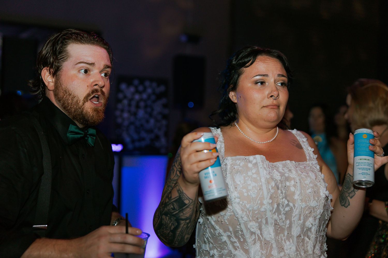 Bride in lace wedding dress and groom in bow tie holding drinks at wedding reception.