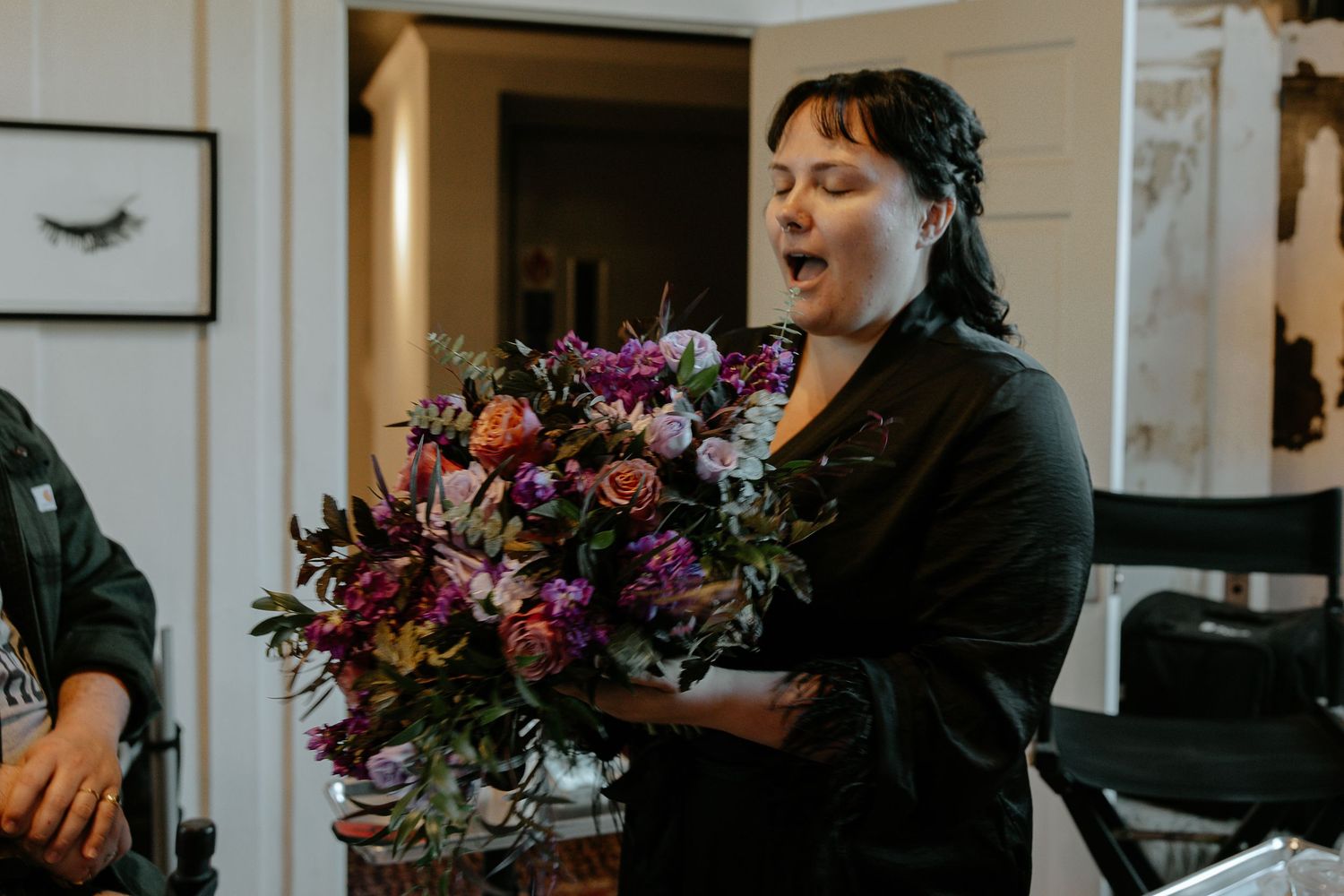 Bride reacts with joy holding a lush purple and orange wedding bouquet indoors.