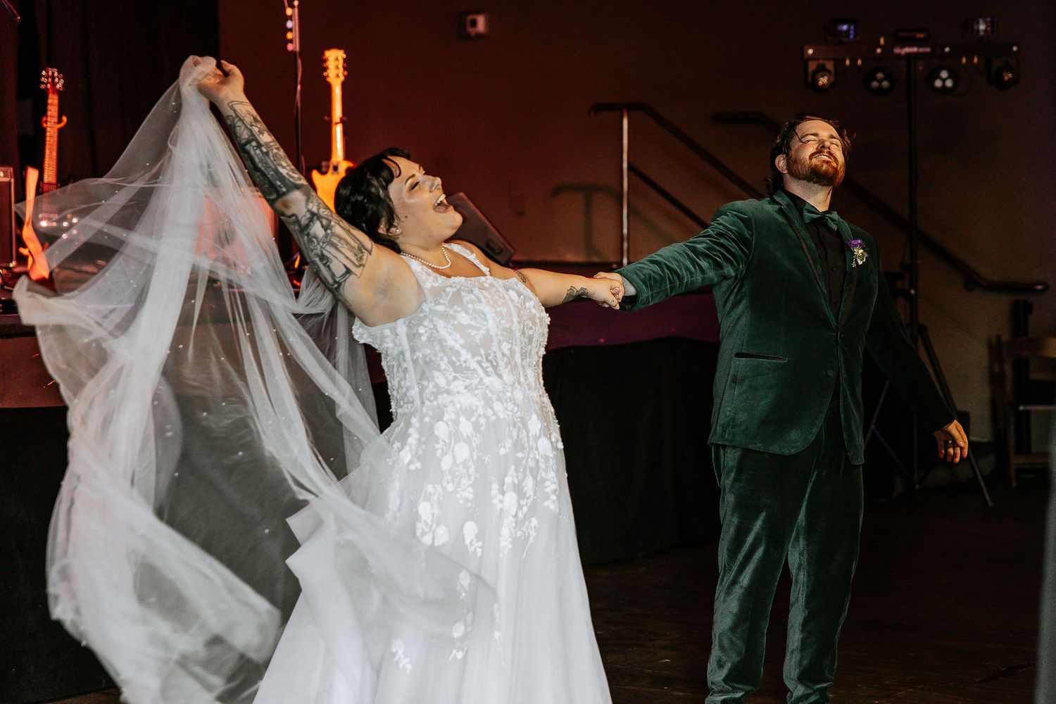 Bride in white veil and groom in green velvet suit dancing at wedding reception.