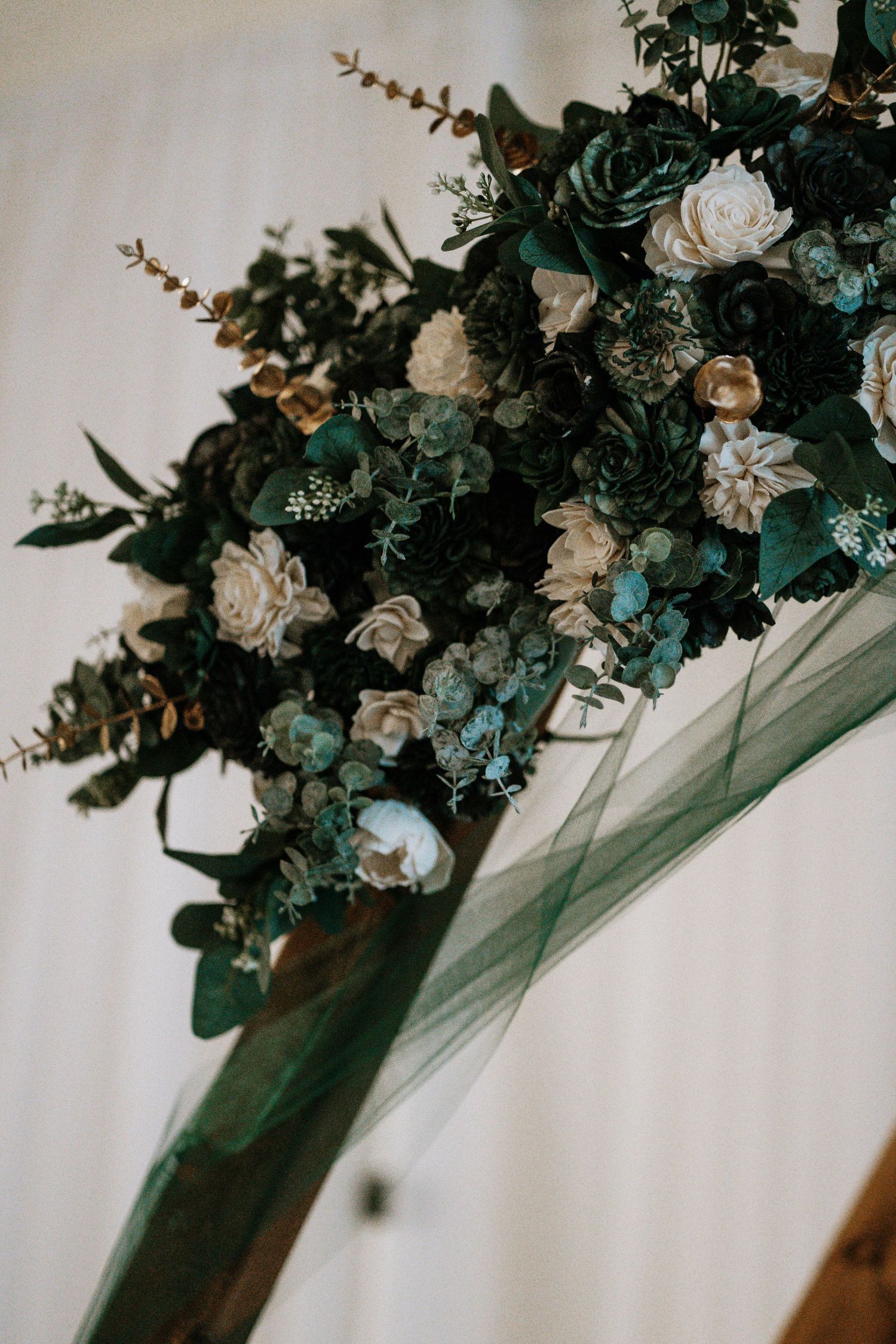 Elegant wedding arch adorned with dark green and ivory flowers, eucalyptus, and flowing emerald tulle fabric.