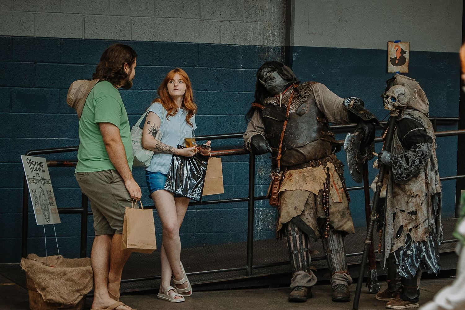 Two people interact with costumed characters in elaborate fantasy costumes at an indoor convention event.