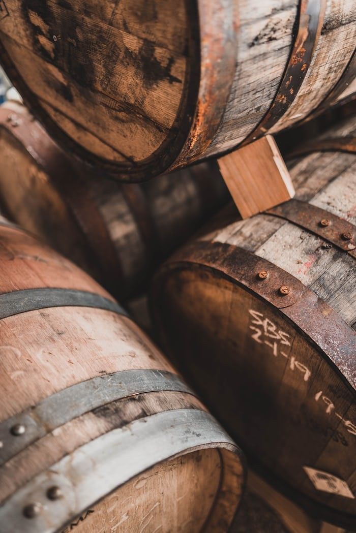 Rustic wooden wine or whiskey barrels stacked together in a cellar, featuring metal bands and aged oak wood texture.