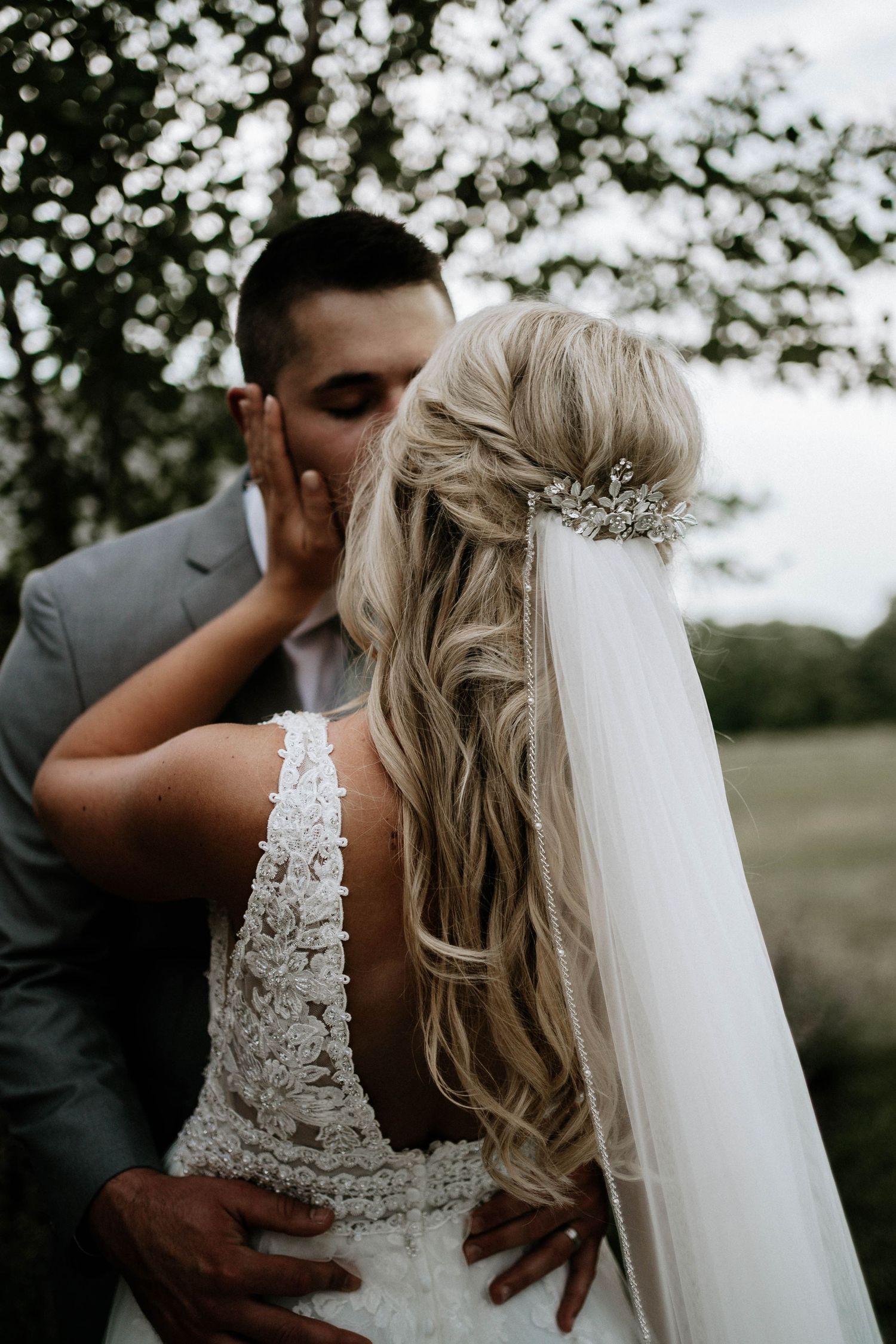 Groom kissing bride on cheek, showcasing brides half-up hairstyle with crystal hair comb and veil.