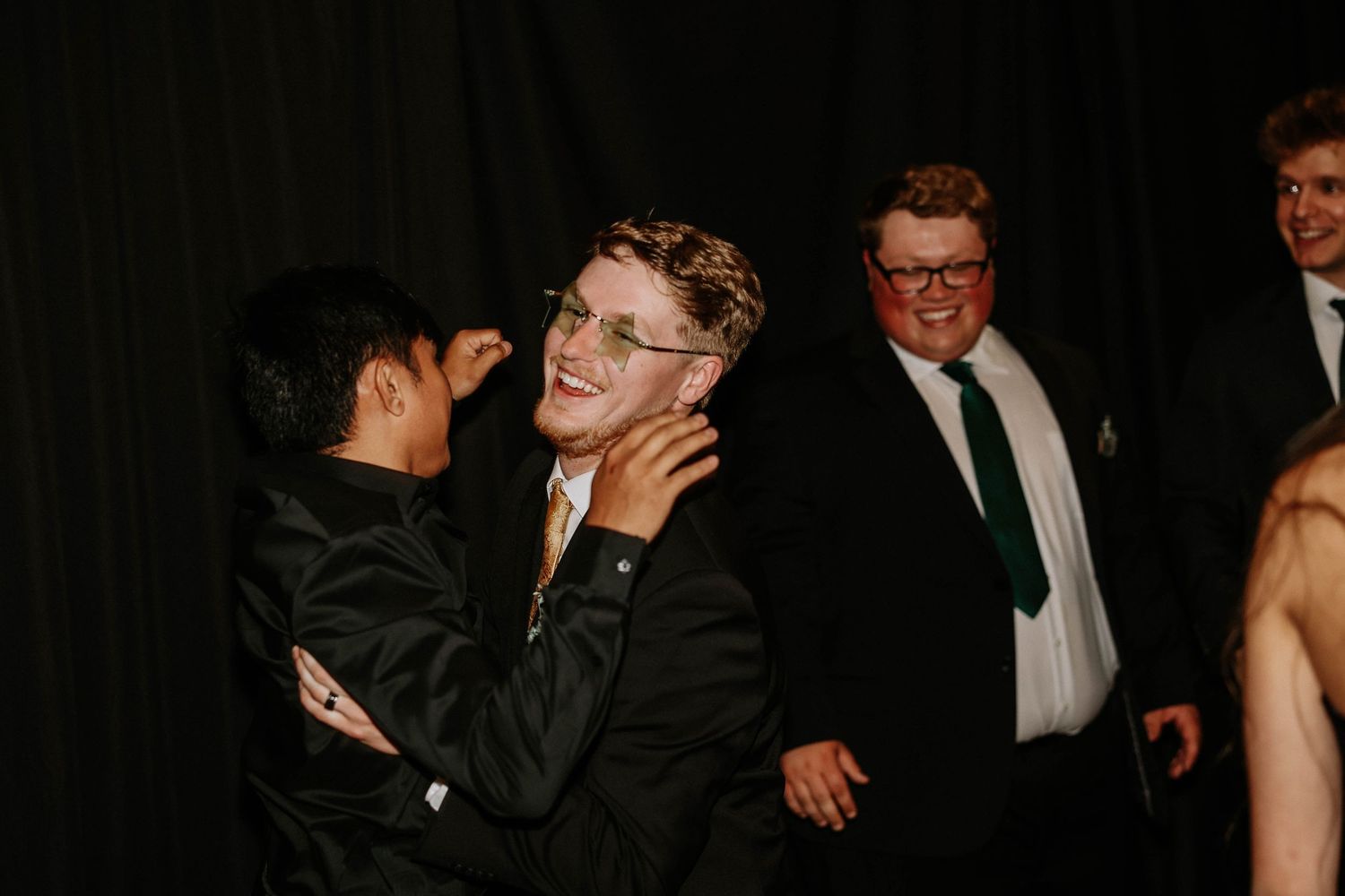 Young men in suits and ties laughing and socializing at a formal event or prom celebration.
