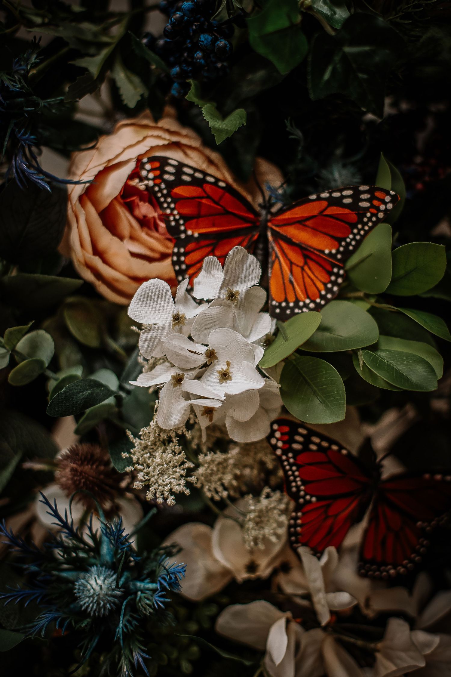 Two vibrant monarch butterflies rest on a lush floral arrangement with roses, white blooms, and green foliage.