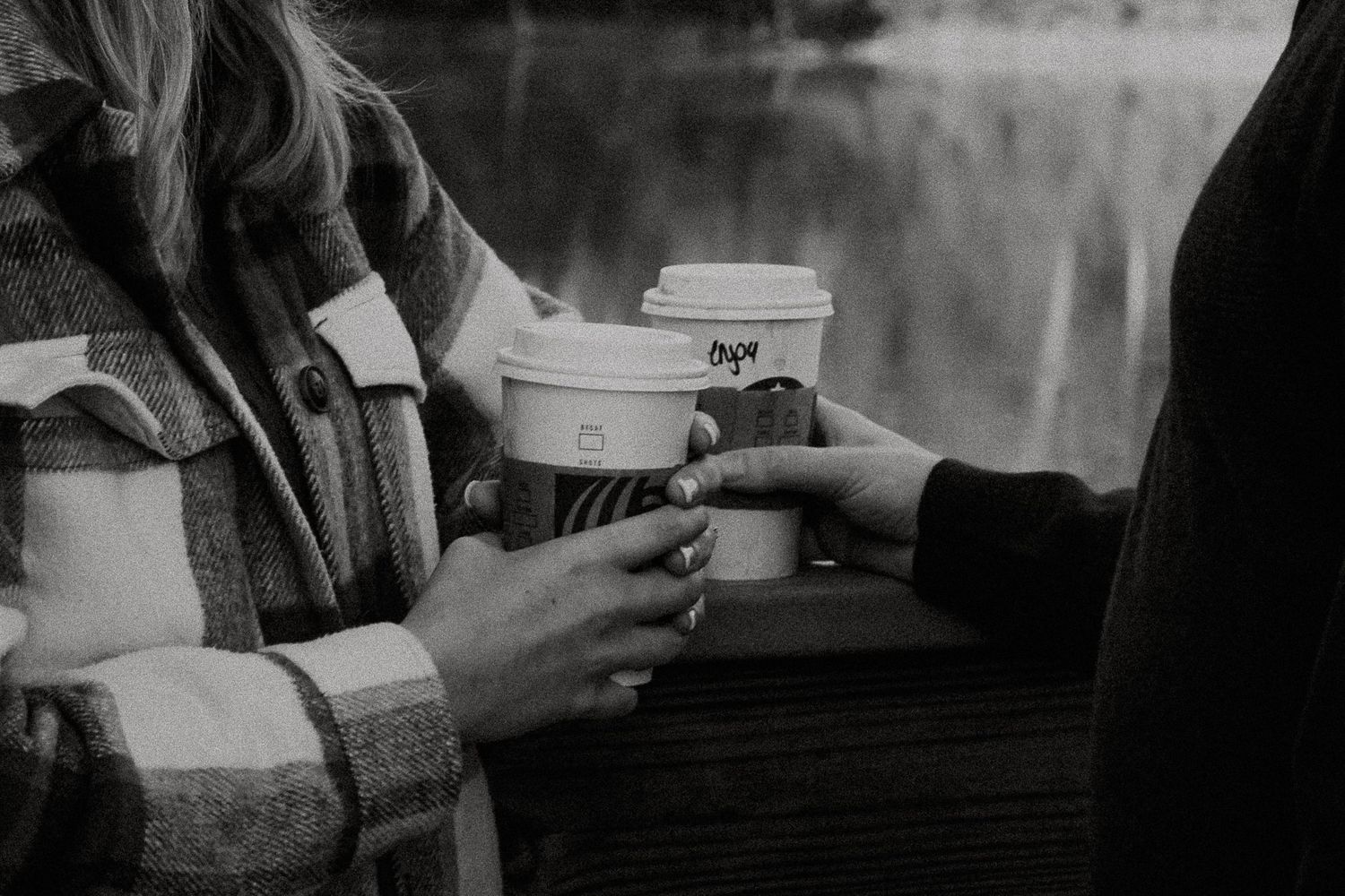 Two people share coffee cups near a lake in a romantic black and white close-up photo in Cincinnati, Ohio
