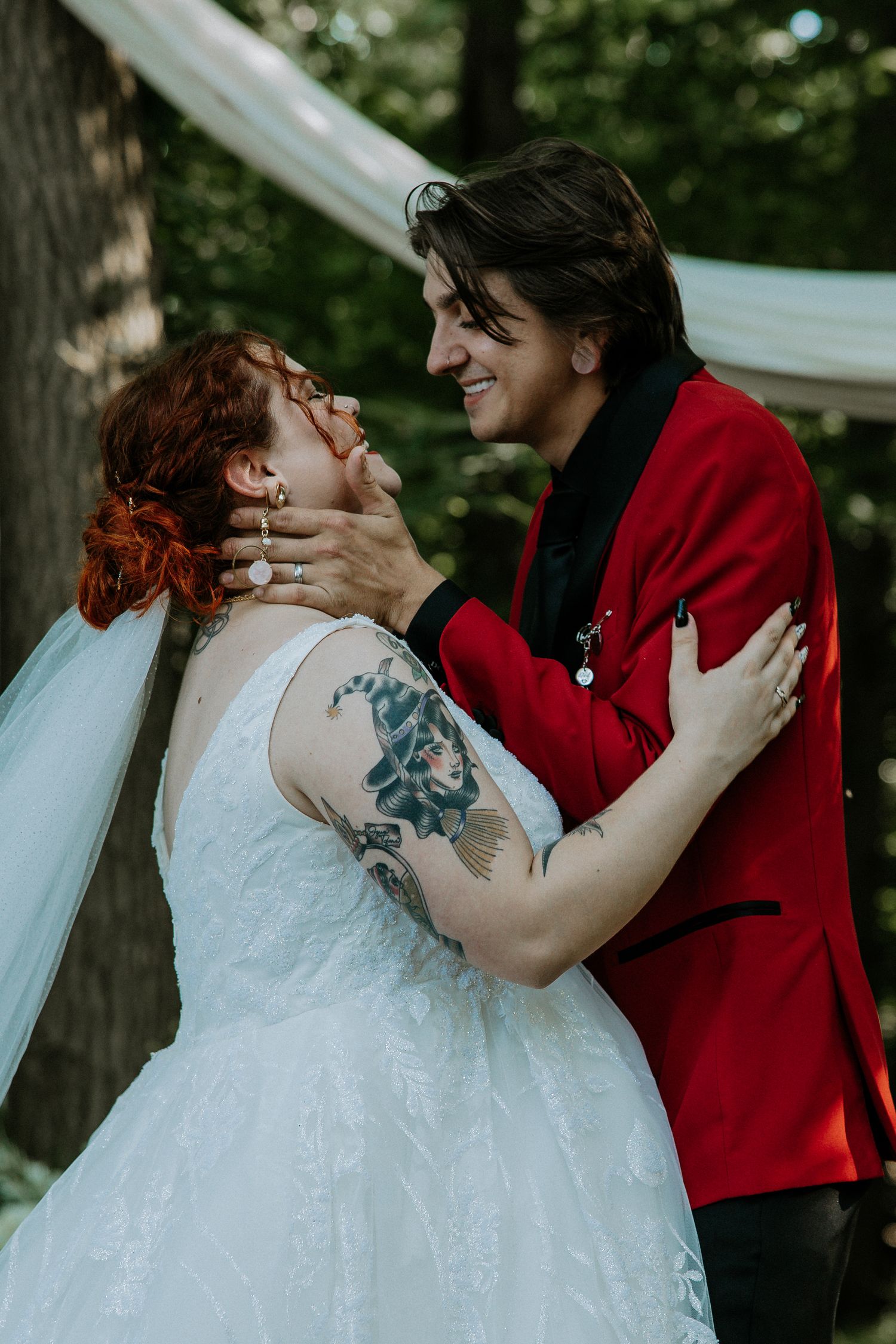 Bride and groom under arch, bride with floral tattoo sleeve, groom in red blazer at the Bella Amore on Enchanted Acres in Dennison, Ohio
