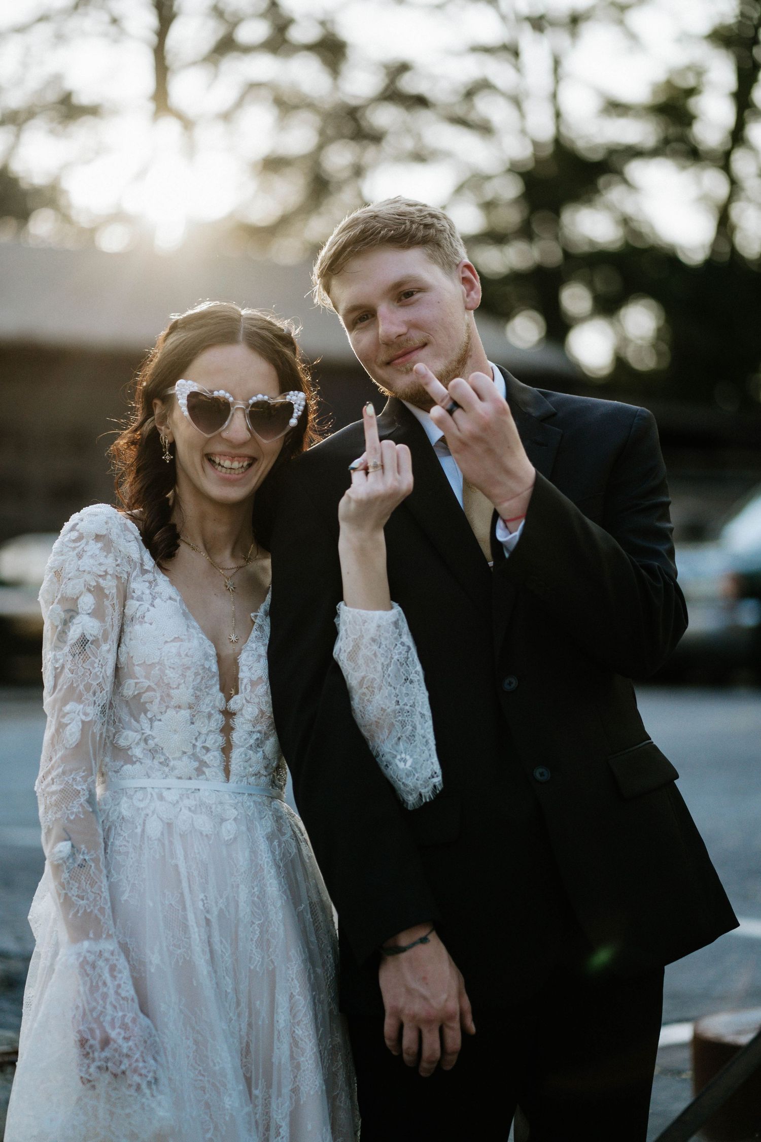 Happy newlyweds in wedding attire wearing heart sunglasses giving playful gesture at golden hour reception at The Brightside in Dayton, Ohio