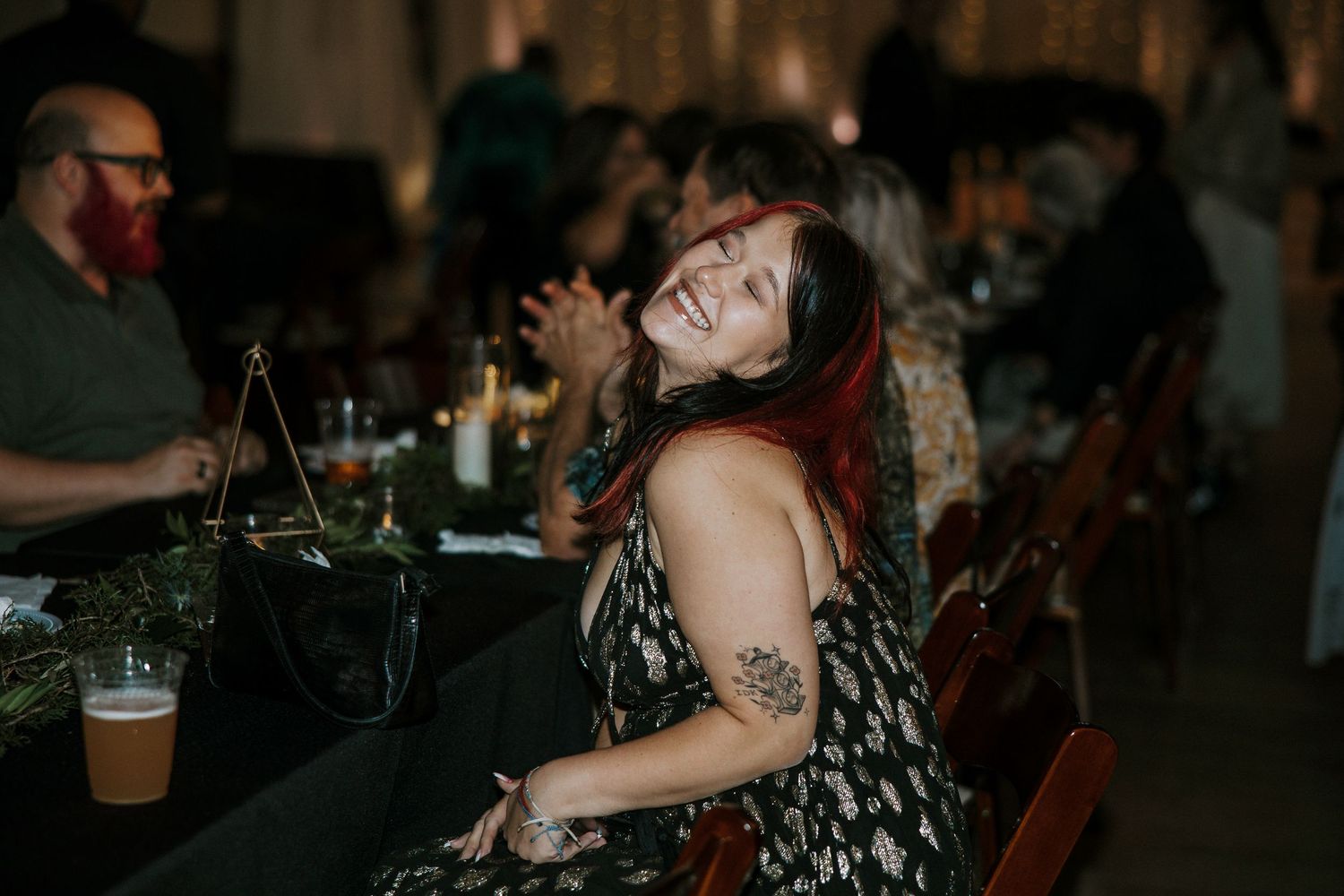 Joyful wedding guest laughing heartily at a decorated reception table with candles and greenery at Urban Artifact in Cincinnati, Ohio