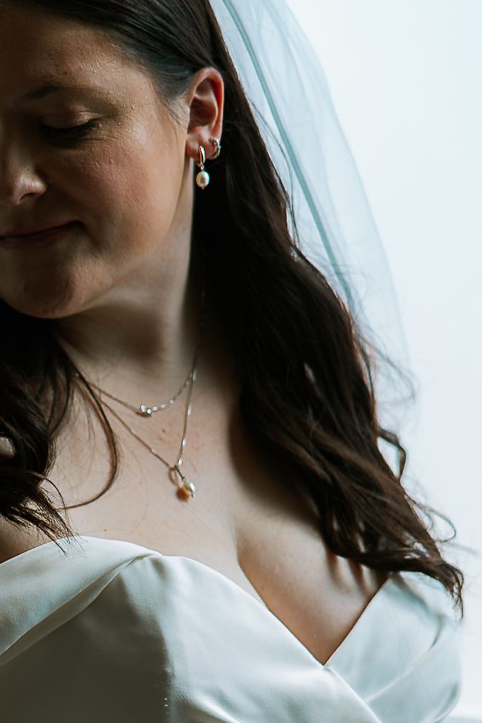 Close-up of bride wearing layered pearl necklaces and gold earrings with veil on wedding day.