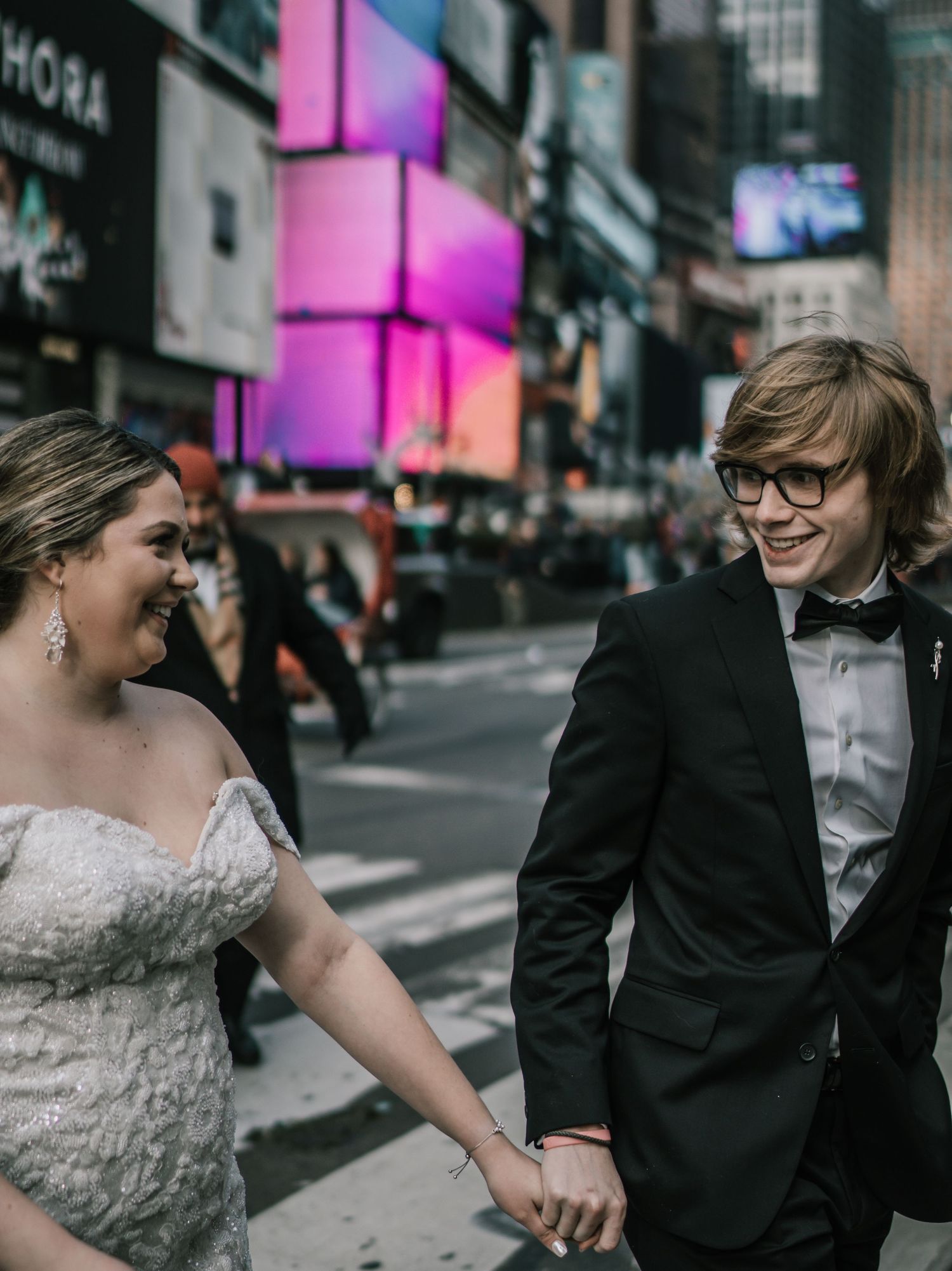 Joyful bride and groom walking hand in hand through Times Square NYC, laughing together in wedding attire.