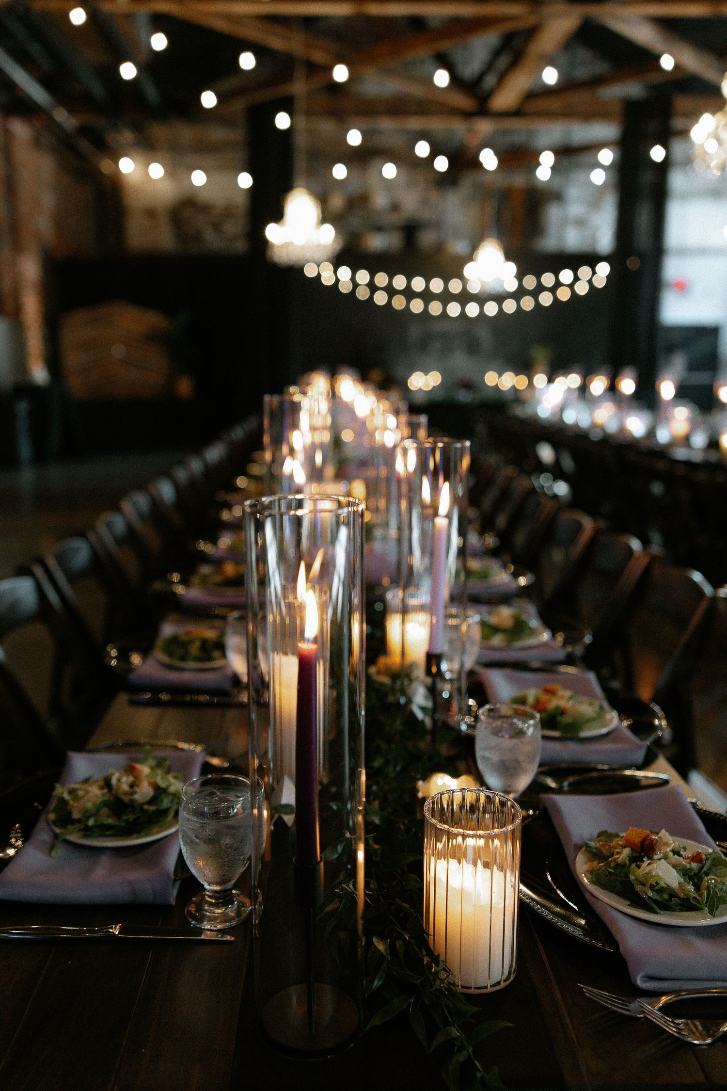 Romantic candlelit wedding reception with long farm tables, greenery runners, and string lights overhead.