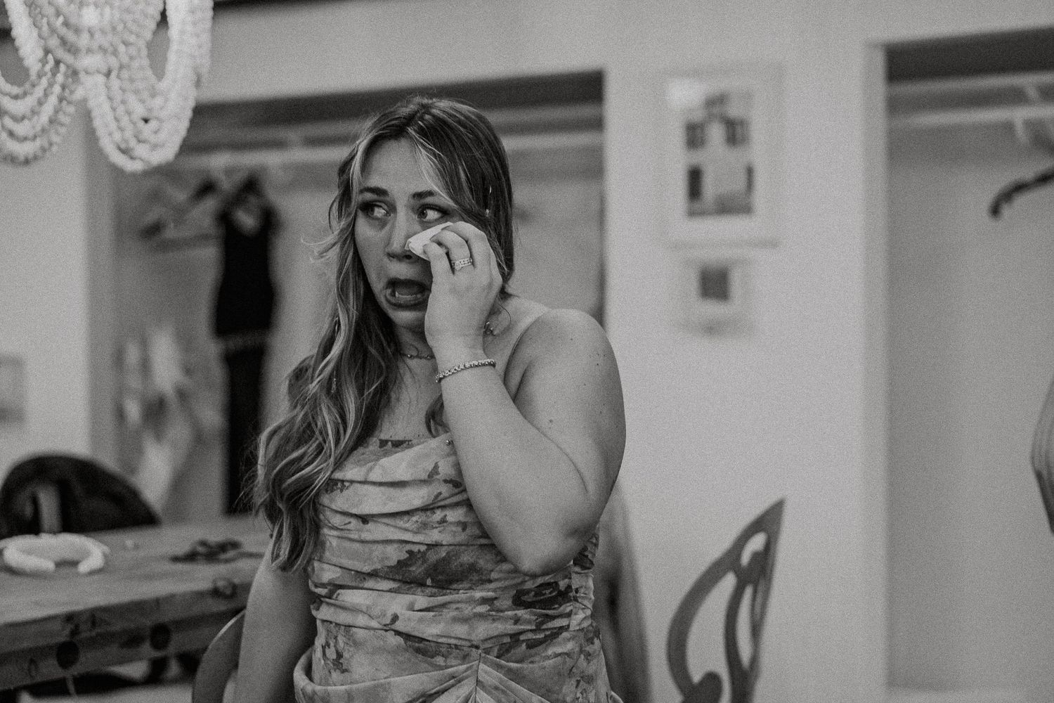 Emotional bridesmaid in floral dress looking surprised in black and white wedding photo.