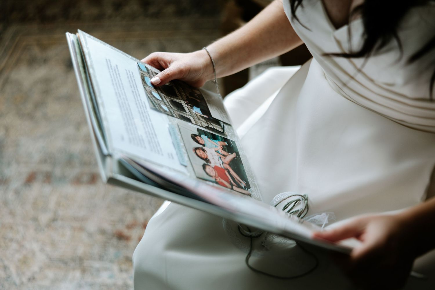 Bride in white dress reading a wedding photo album while seated, showing cherished memories.