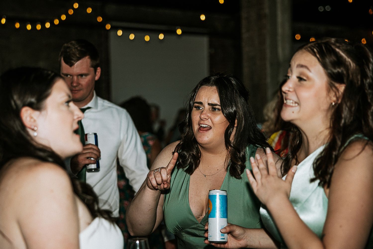 Bridesmaids in mint green dresses laugh and celebrate together on the wedding reception dance floor.