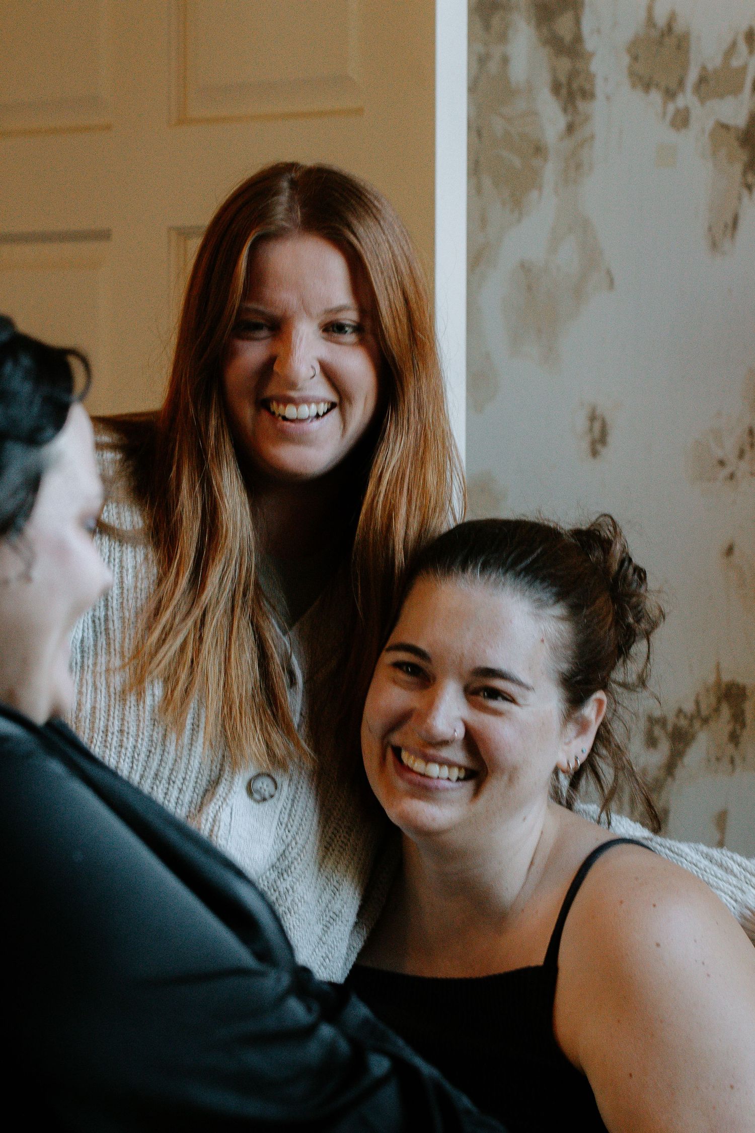 Two bridesmaids smiling and laughing with the bride during wedding preparations.