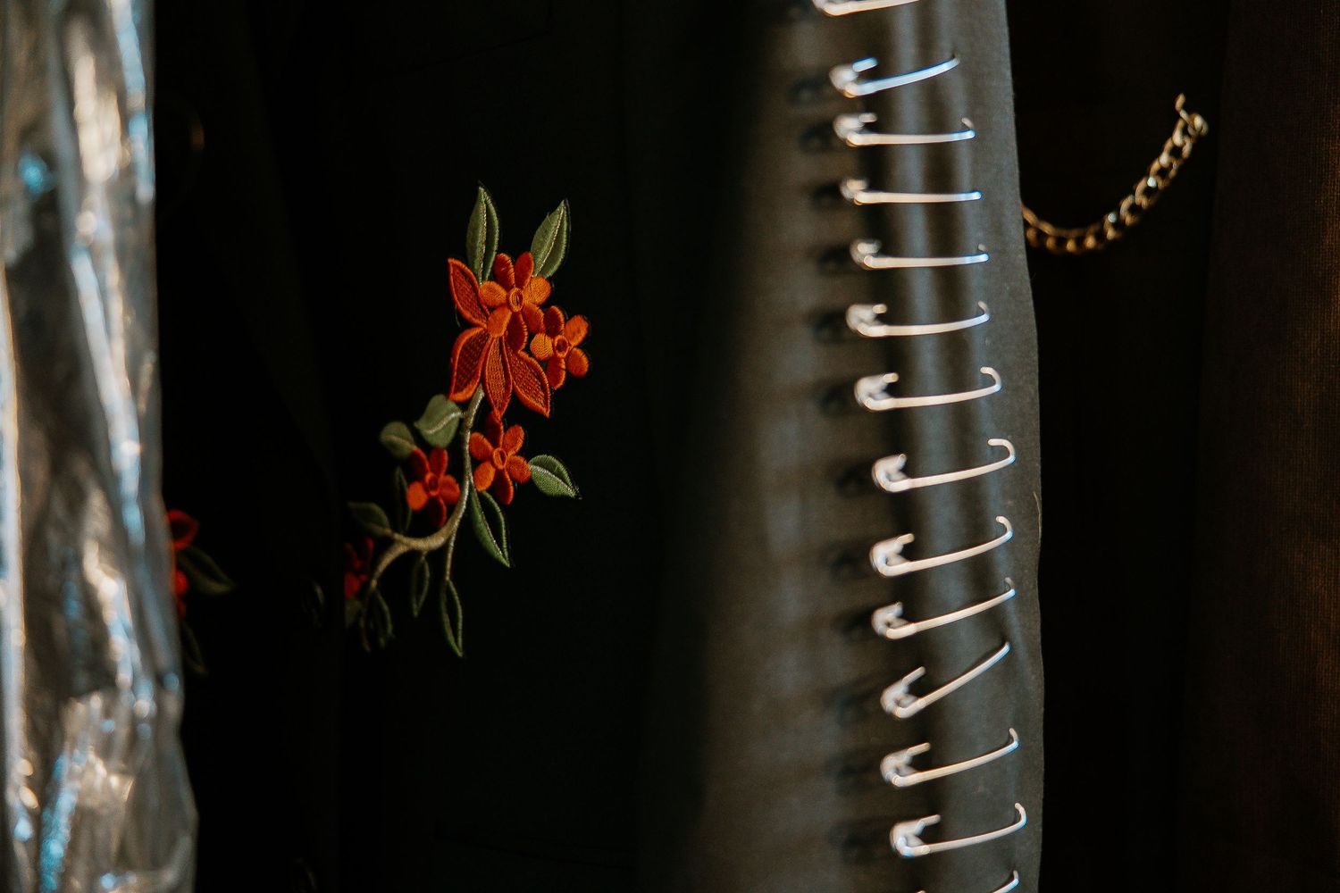 Close-up of a black garment with red floral embroidery and silver lace-up detail.