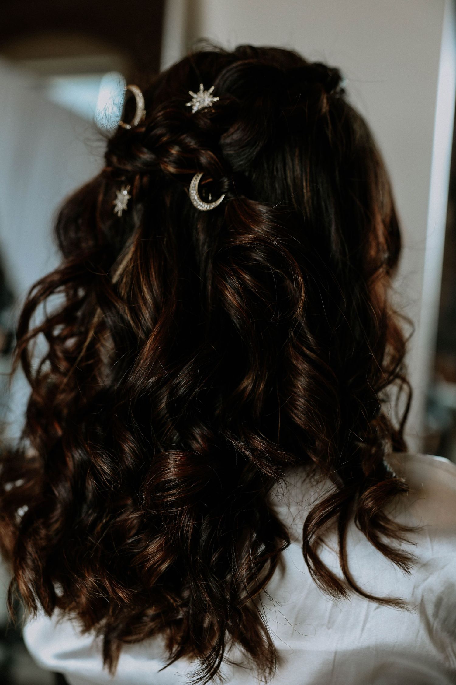 Dark curly half-up hairstyle adorned with silver celestial moon and star hair pins, perfect for a wedding.