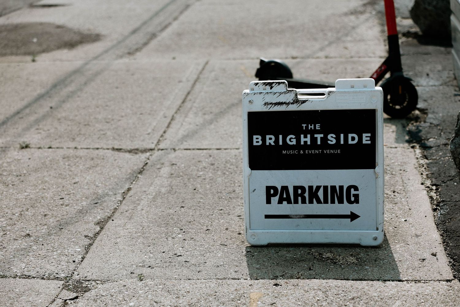A white sandwich board sign for The Brightside music and event venue with a parking arrow on a city sidewalk.
