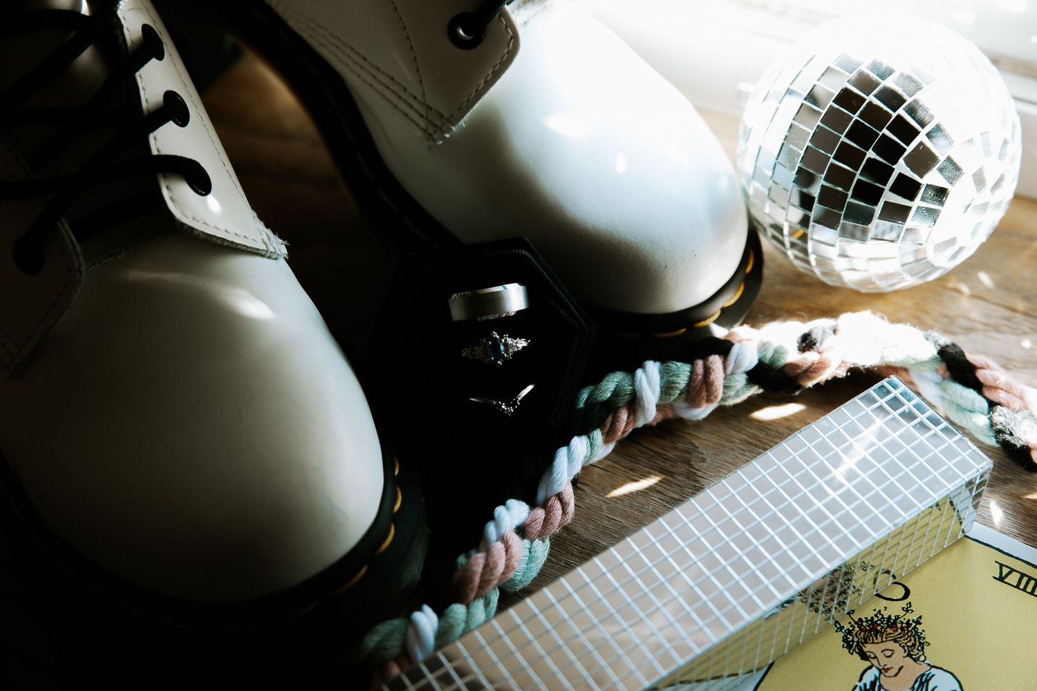 White Doc Martens boots beside a disco ball and colorful braided rope on a wooden surface.