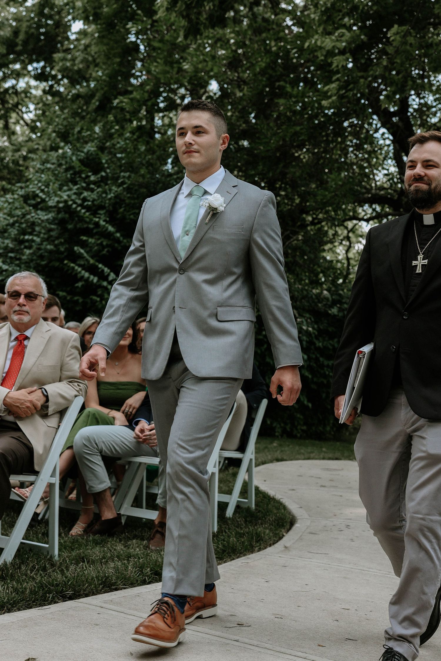 Groom in gray suit with mint tie walks down the aisle at an outdoor wedding ceremony.