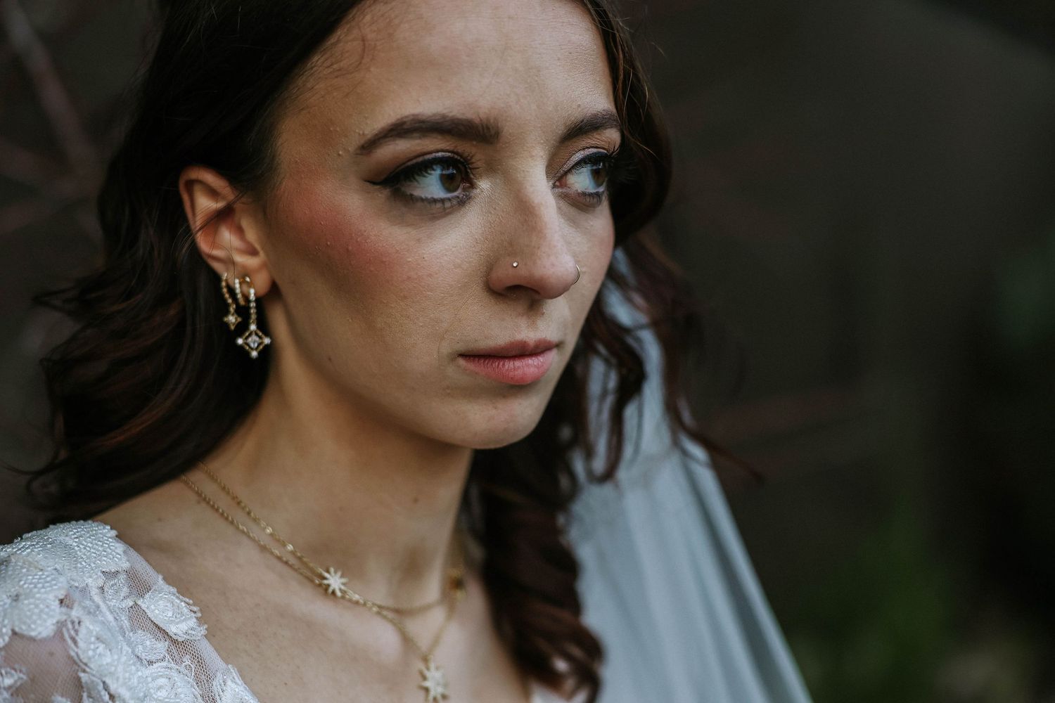 Close-up portrait of a bride wearing gold star earrings, necklace, and veil with elegant wedding makeup.