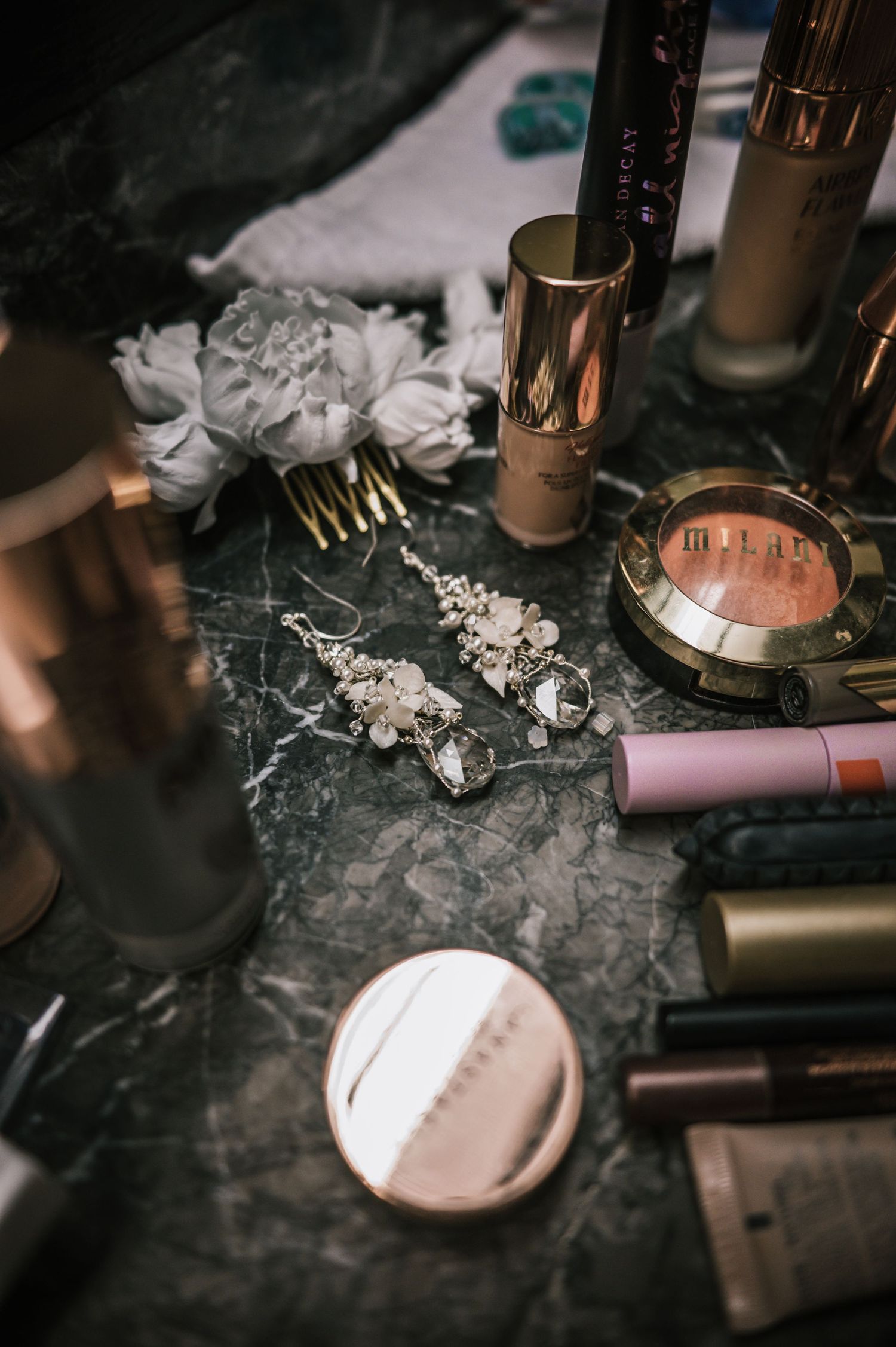 Bridal accessories with crystal earrings, hair comb, and makeup on marble vanity.
