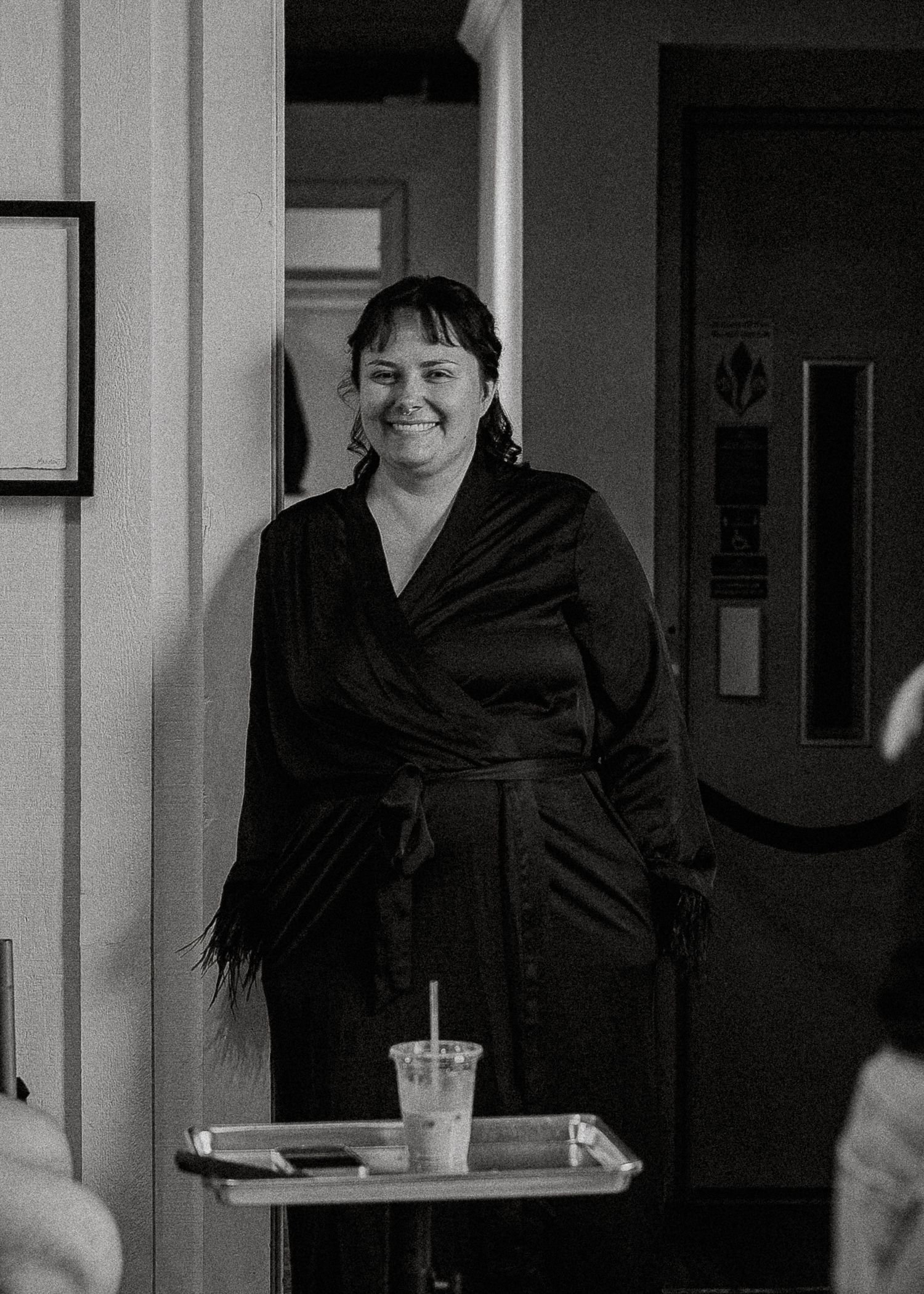 Black and white portrait of a smiling woman in a black wrap dress indoors.