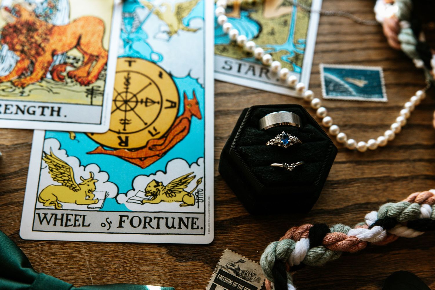Wheel of Fortune tarot card with engagement rings in black velvet box and pearl necklace.