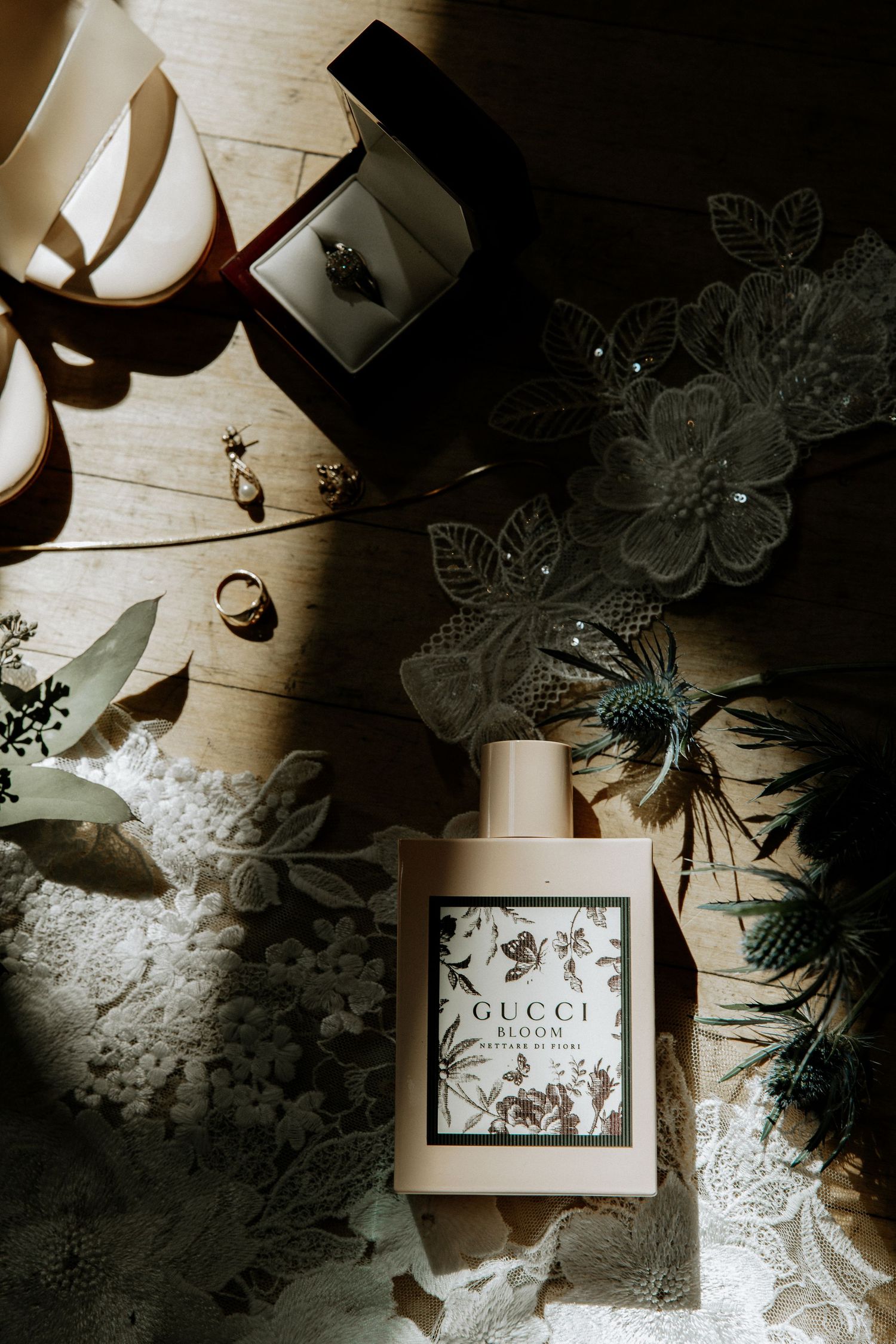 Gucci perfume bottle displayed in a bridal flat lay with rings, earrings, and blue thistle flowers at Urban Artifact in Cincinnati, Ohio
