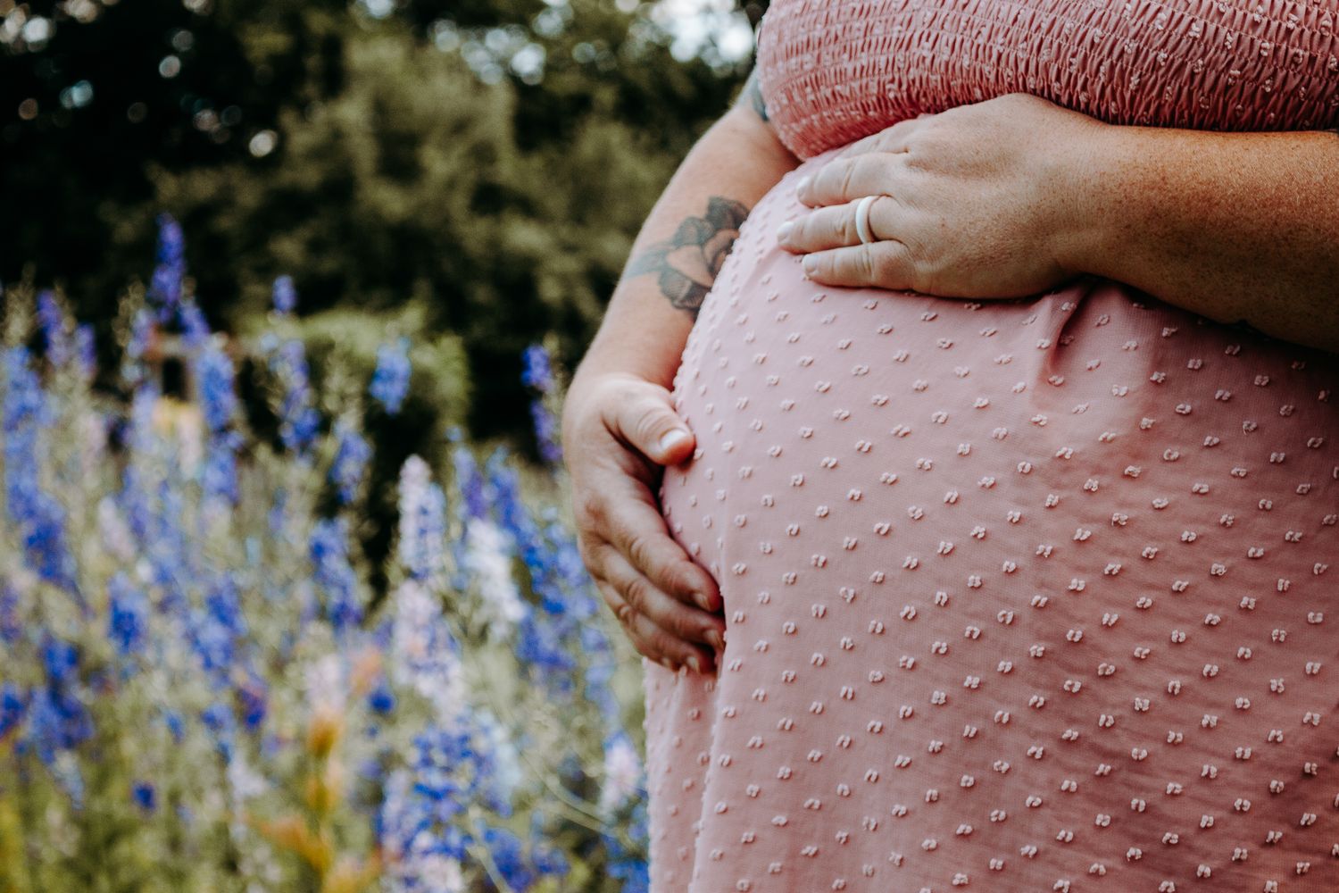 Close-up of a pregnant woman in a pink dress cradling her baby bump outdoors in Downtown Yellow Springs, Ohio