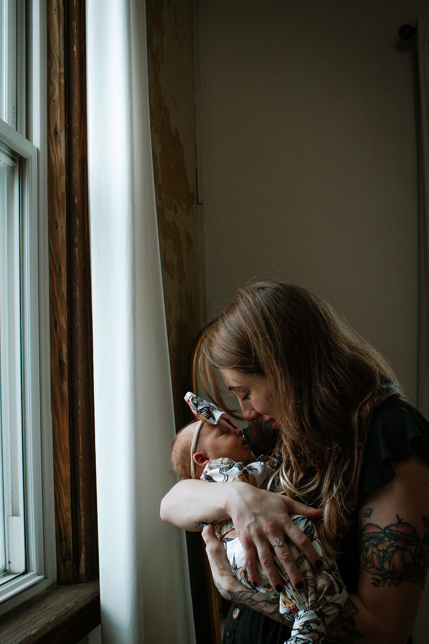 Tattooed mother tenderly kissing newborn baby by window in Cincinnati, Ohio.