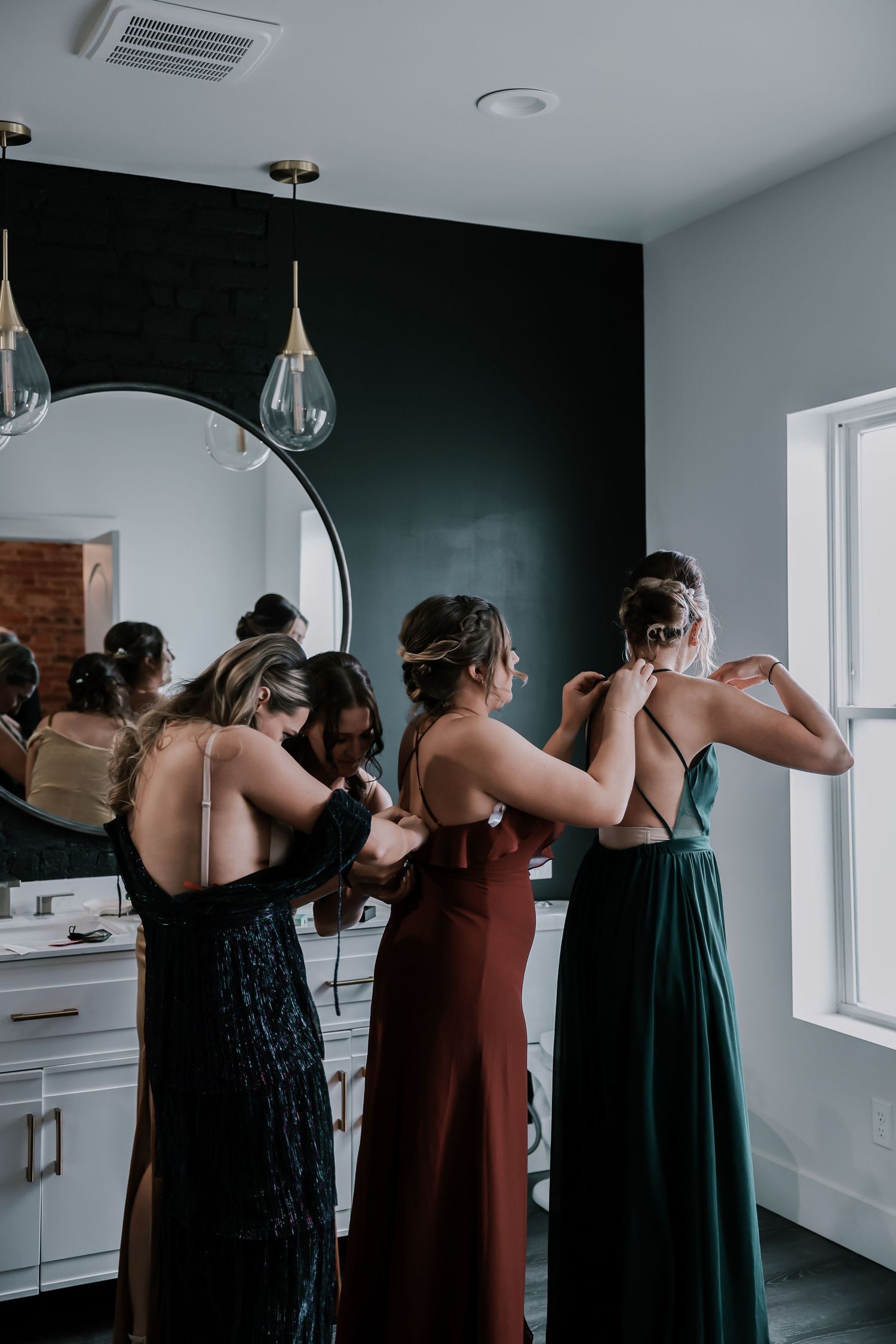 Bridesmaids in jewel-toned dresses helping each other get ready before wedding ceremony in modern bathroom at The Vue in Columbus, Ohio