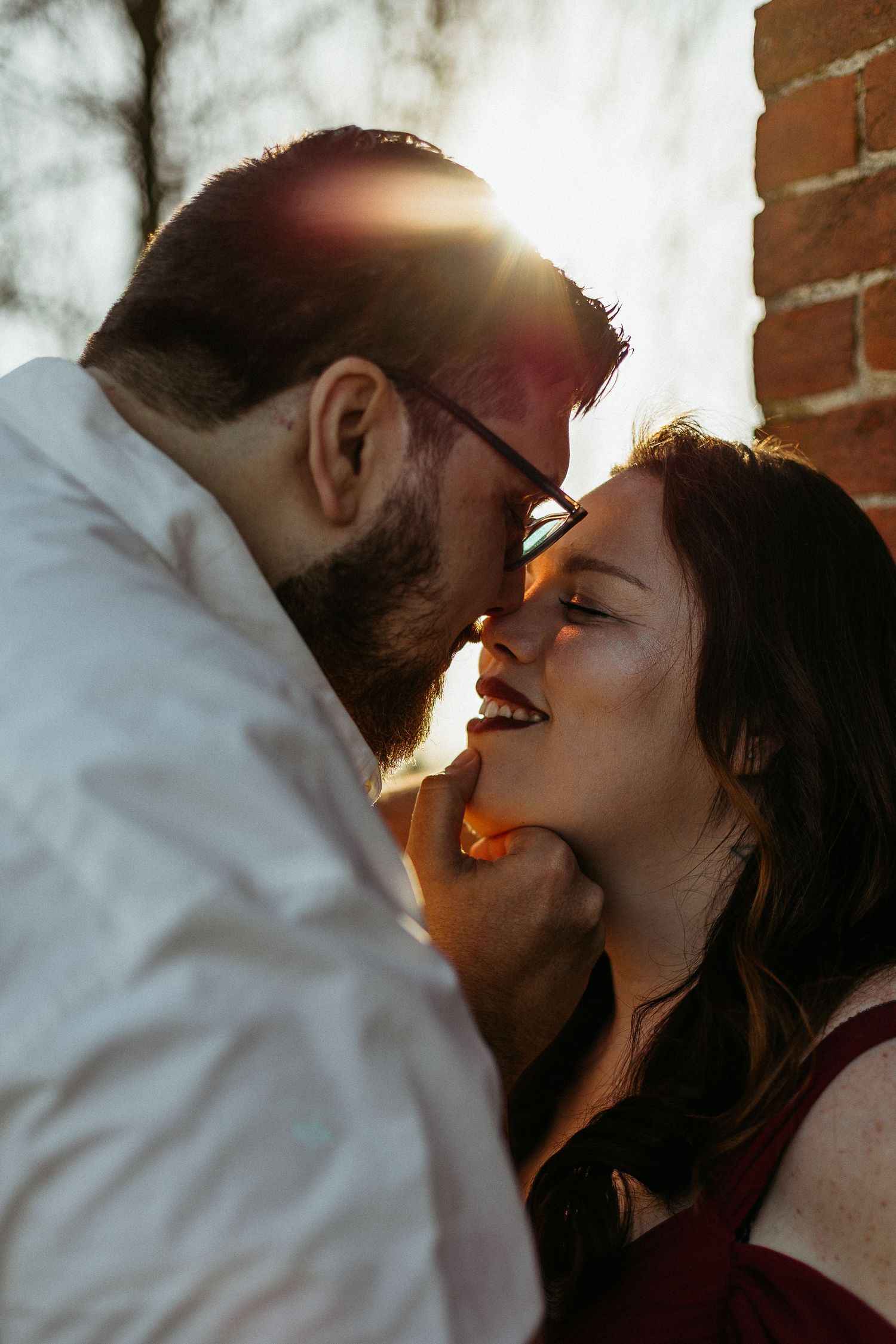 Couple sharing a romantic moment in golden sunset light against a brick wall outdoors.