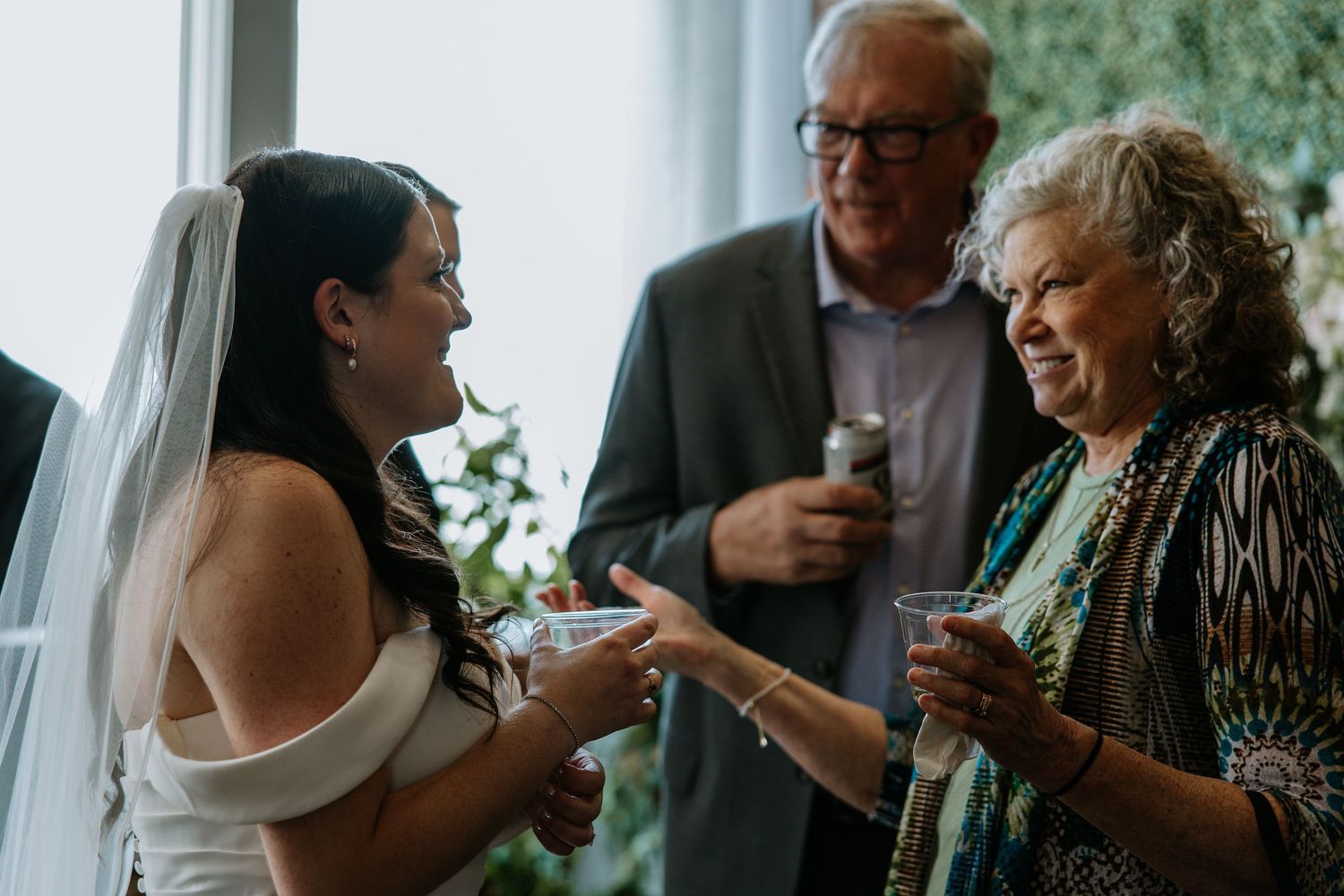 Bride in white off-shoulder gown sharing a moment with elderly guests at wedding.