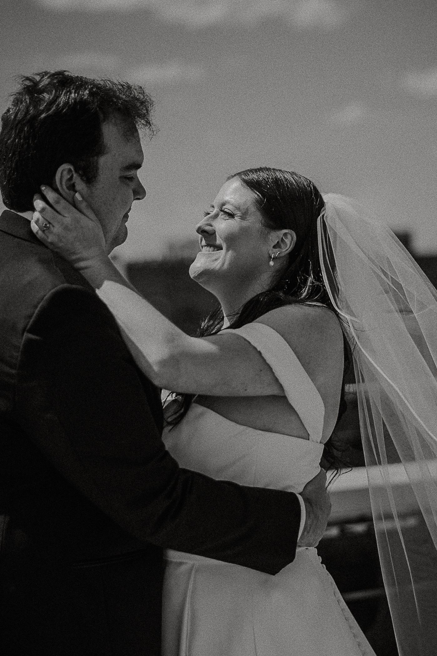 Black and white photo of laughing bride embracing groom after wedding ceremony on a rooftop.