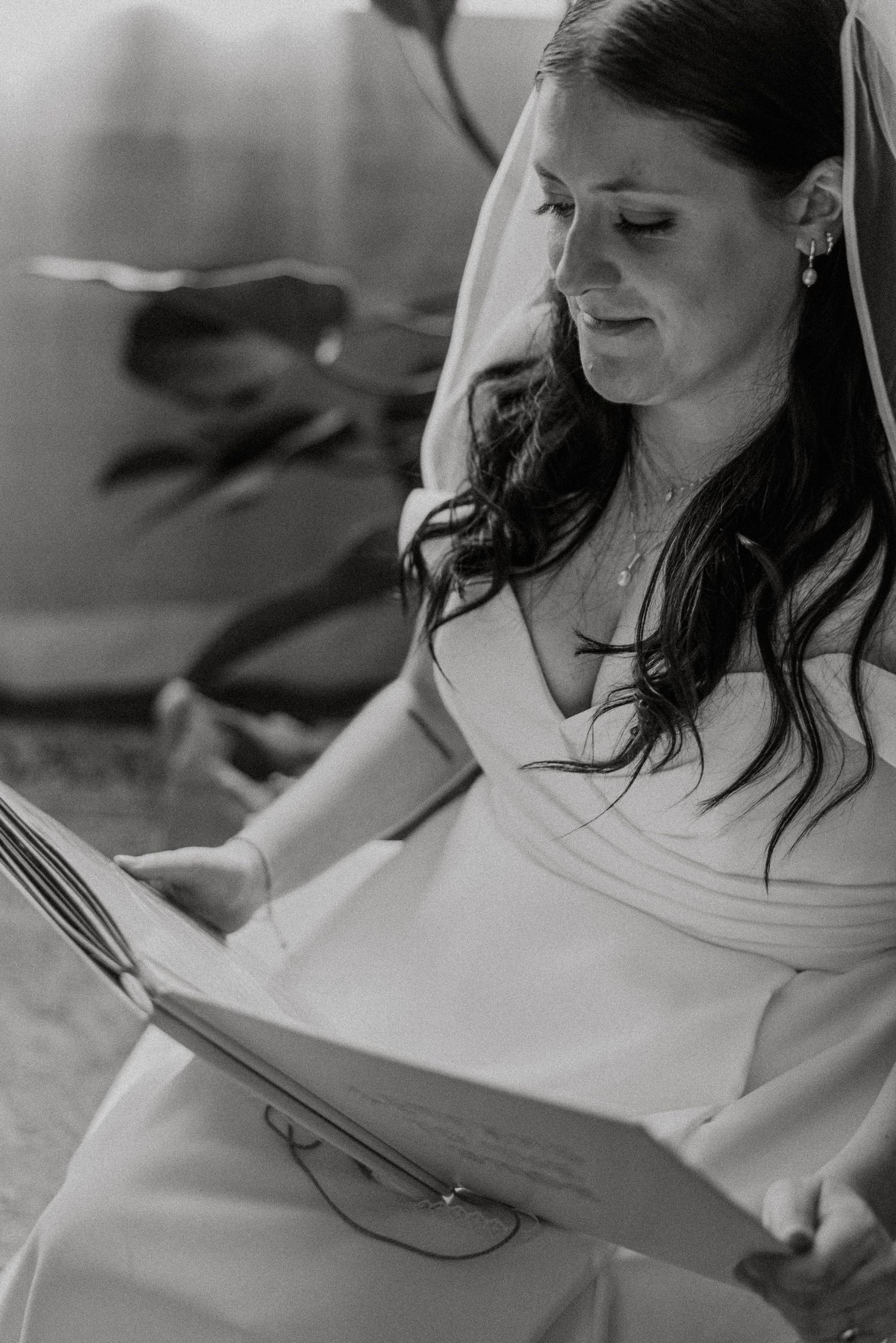 Black and white photo of bride in veil and gown emotionally reading a letter.