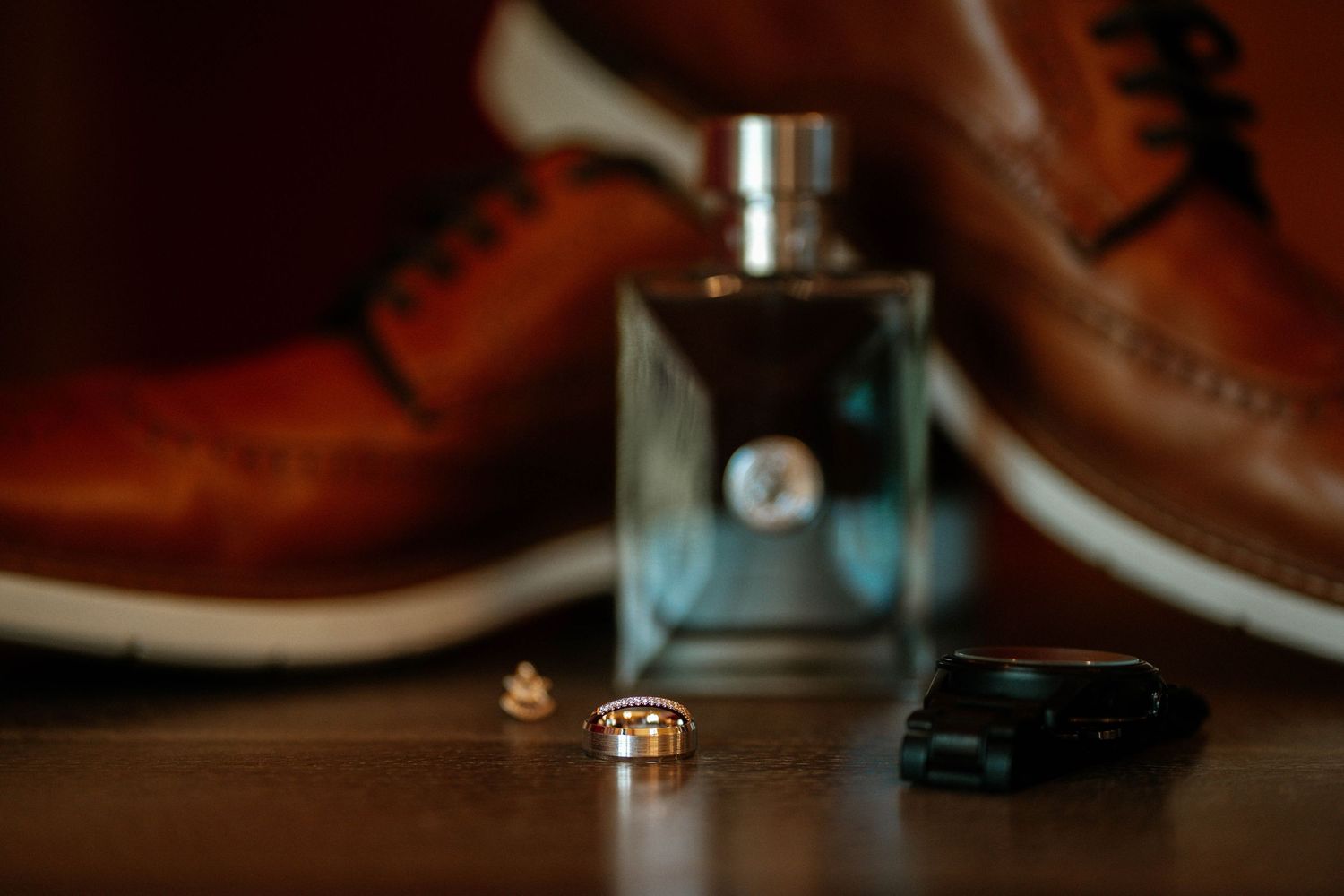 Grooms wedding details flat lay featuring cologne, gold ring, cufflinks, and brown leather dress shoes.