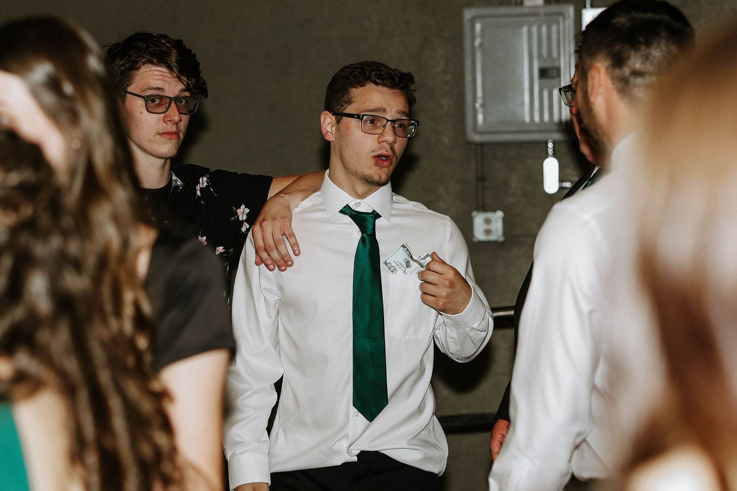 Young man in white shirt and green tie socializing with friends at a formal event or dance.