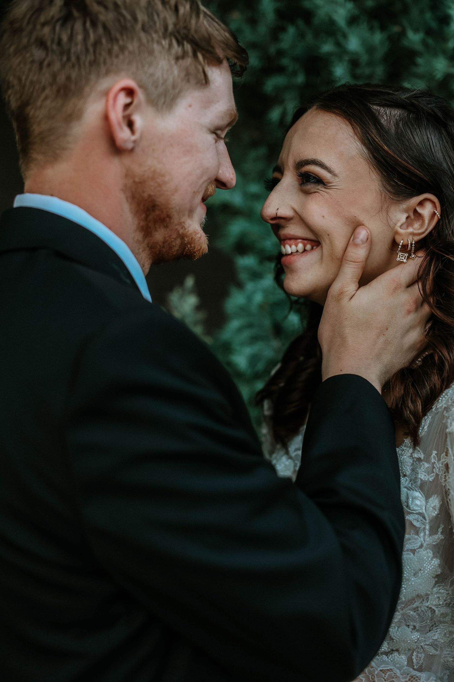 A groom tenderly cups his smiling bride's face during an intimate outdoor wedding portrait moment.