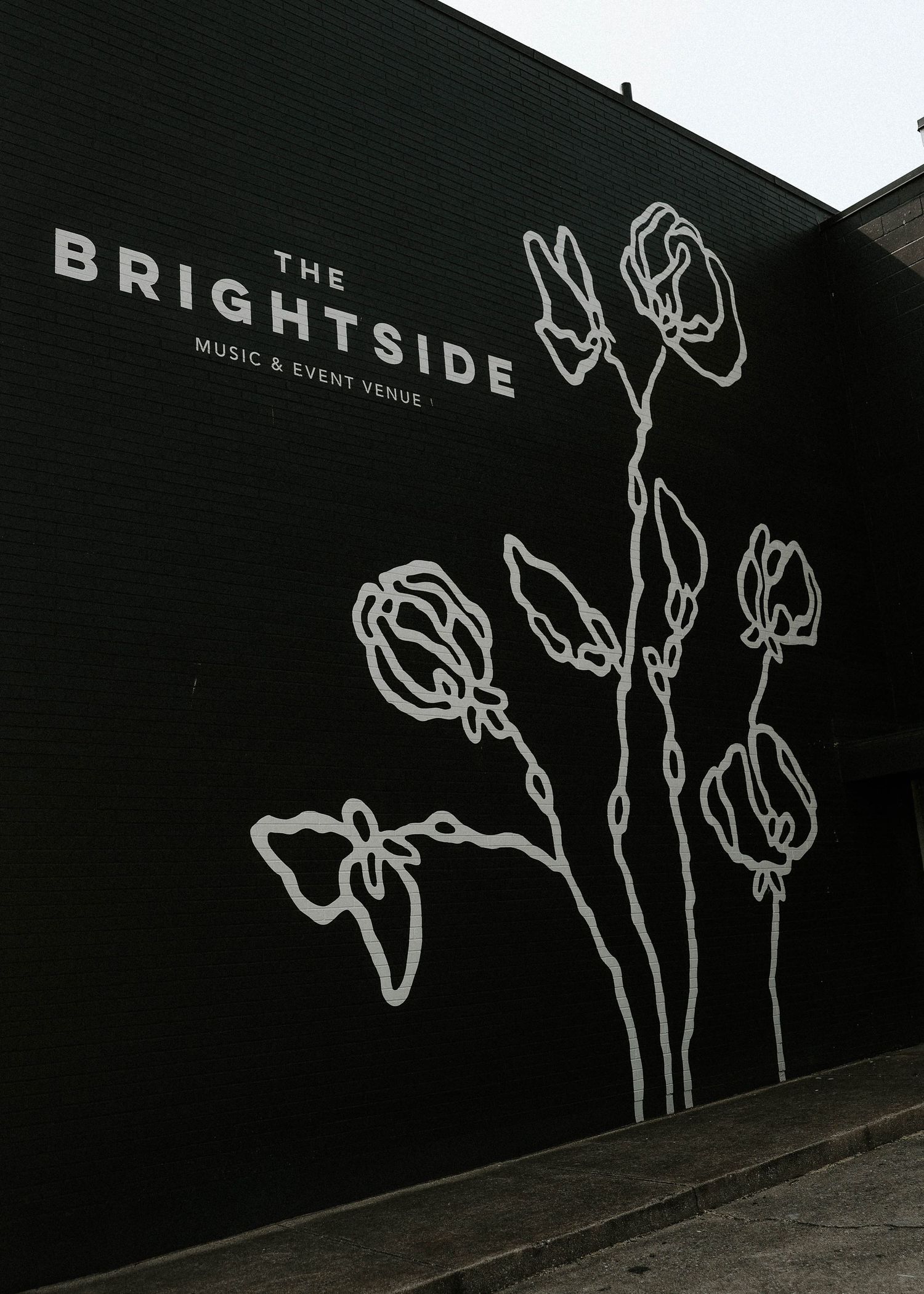 Black wall mural of The Brightside Music & Event Venue sign with white floral line art drawings.