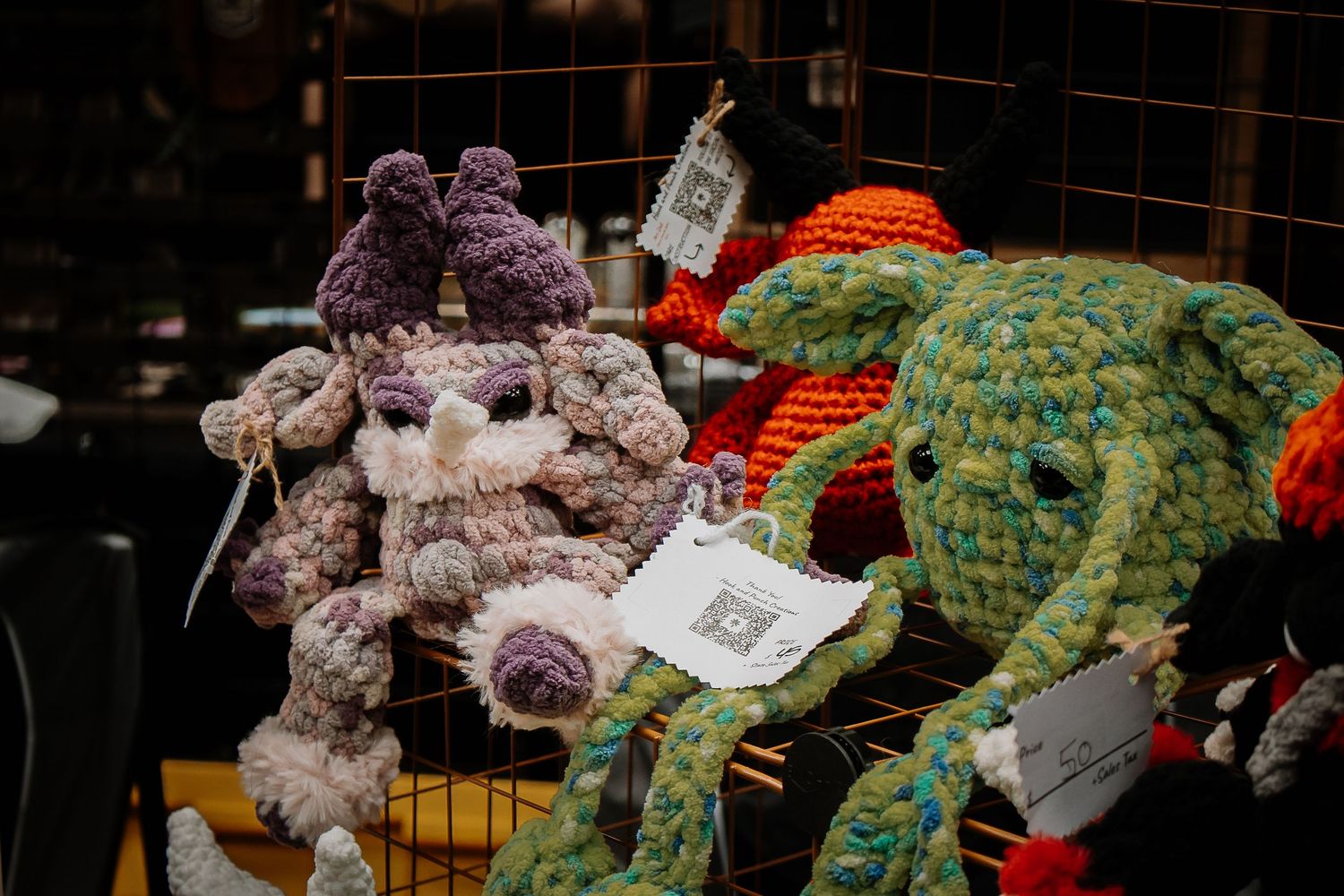 Handmade crocheted animal stuffed toys displayed on a wire rack at a craft market.