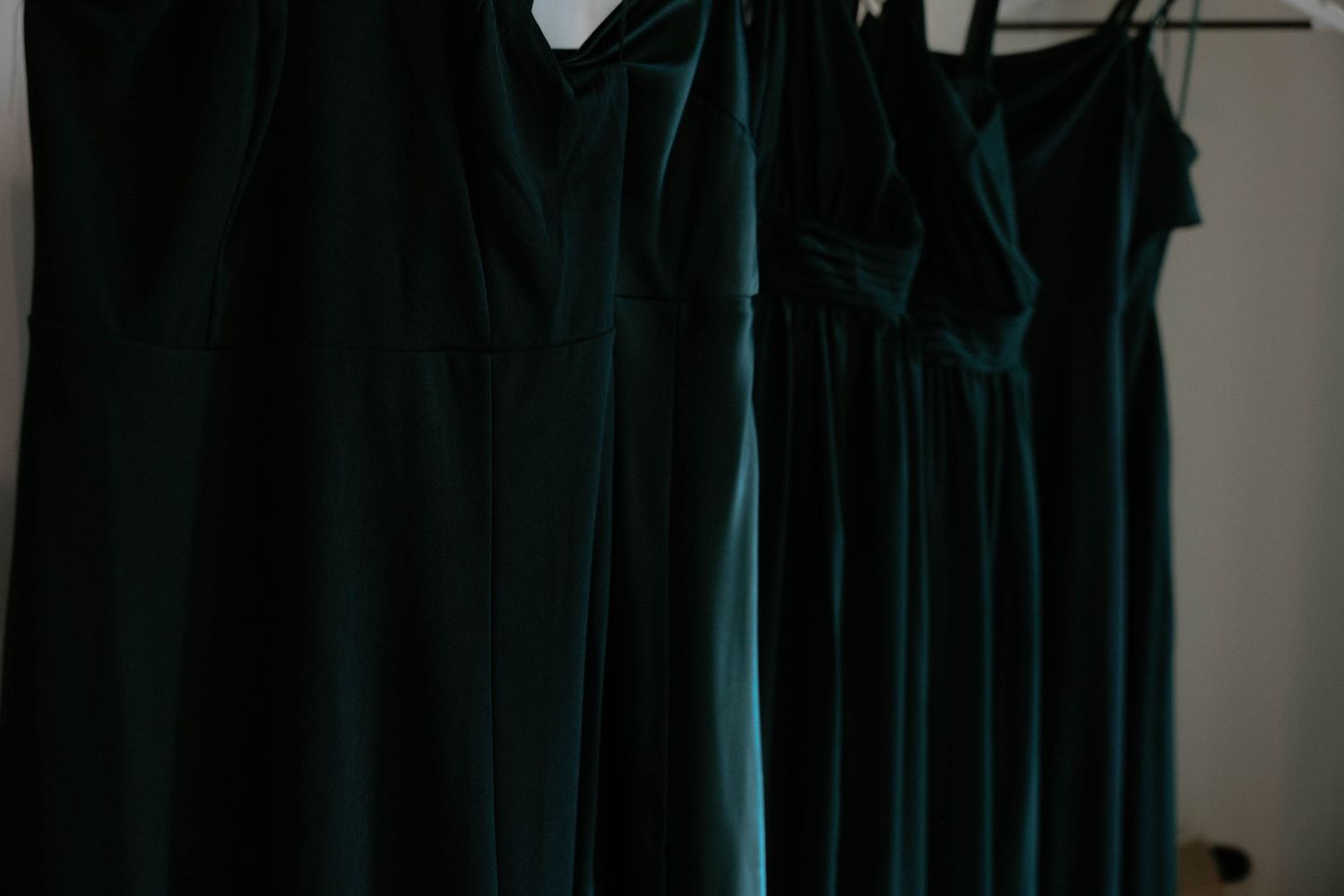 Three emerald green velvet bridesmaid dresses hanging on rack before wedding ceremony.