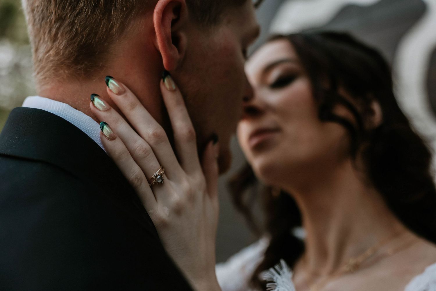 Bride with green nails gently holds groom's face as they share an intimate moment at their wedding.