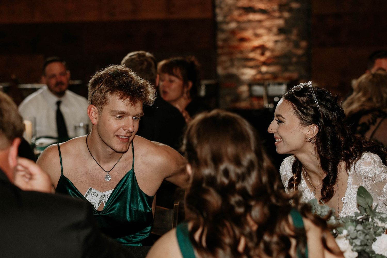 Wedding guests in formal attire share a joyful conversation at a reception, with a smiling bride in a white gown.