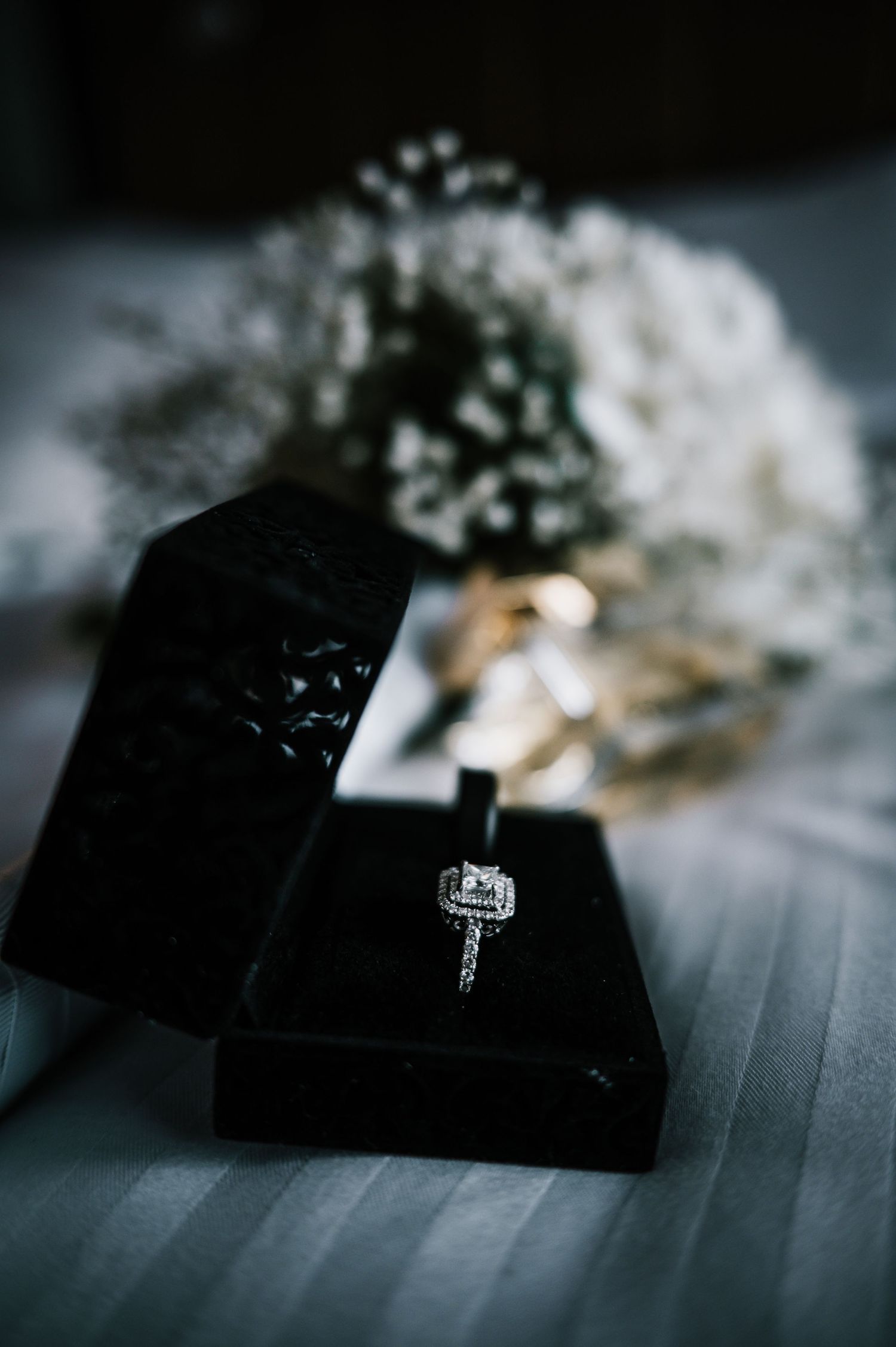 Diamond engagement ring in black velvet box with white floral bouquet background.