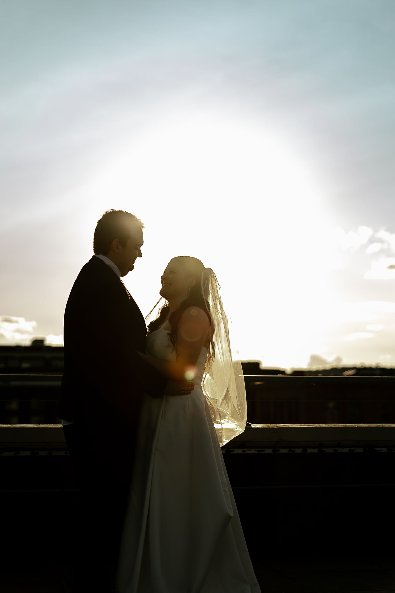 Silhouette of bride and groom embracing at sunset with glowing backlight.