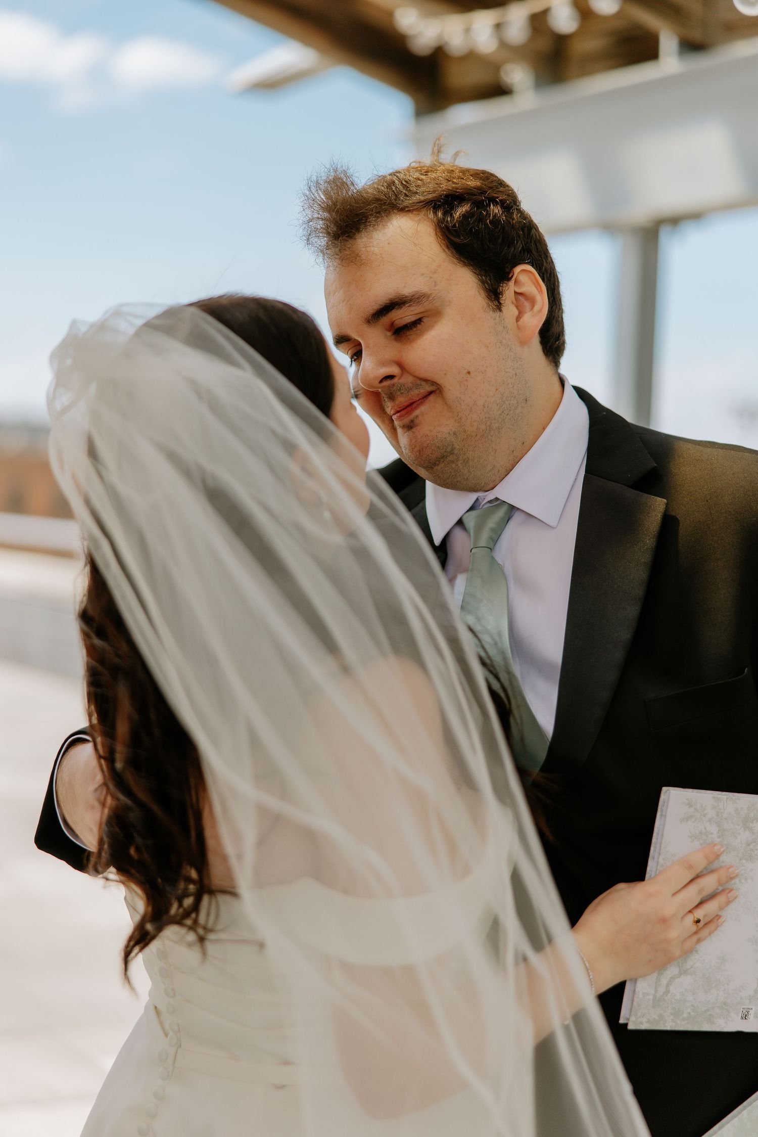 Groom smiles tenderly at bride as they share an intimate moment after exchanging wedding vows outdoors.