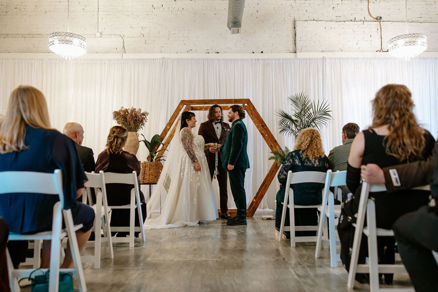 Wedding ceremony with guests seated as couple stands before hexagonal wooden arch altar.