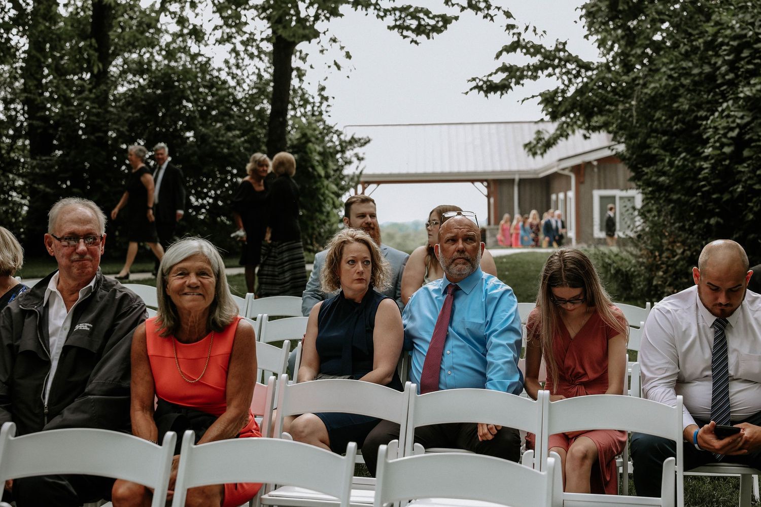 Wedding guests seated in white chairs at an outdoor ceremony on a lush green lawn.